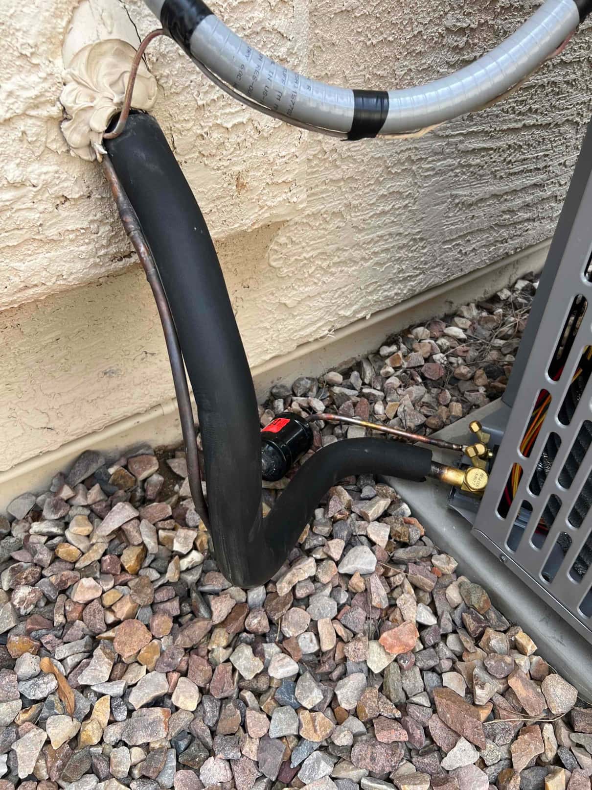 Refrigerant line set exiting wall with insulated suction line, liquid line, and flexible electrical whip connected to the outdoor unit.