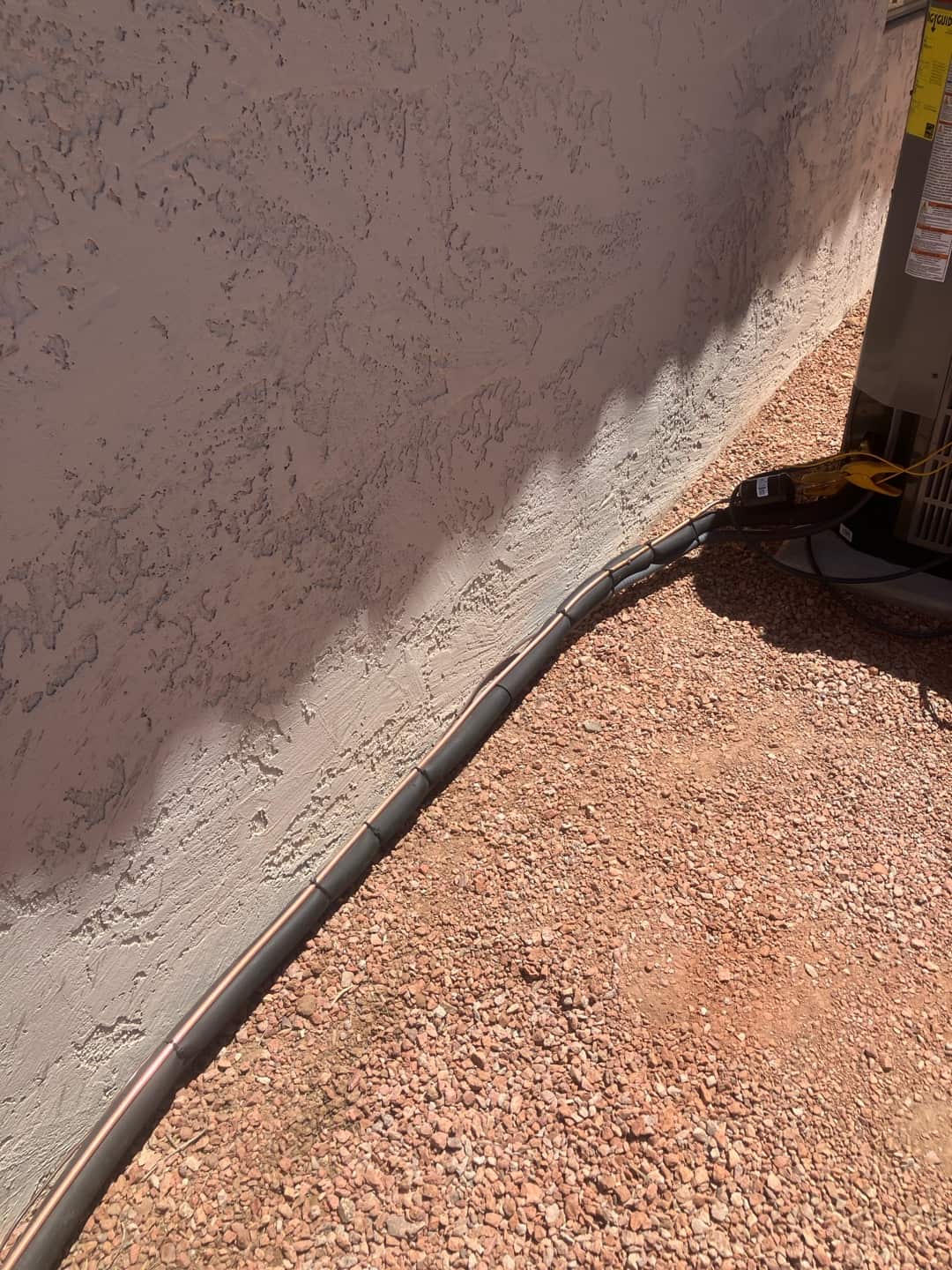 Refrigerant line set with segmented insulation routed neatly along the wall to the outdoor condenser on a gravel surface.