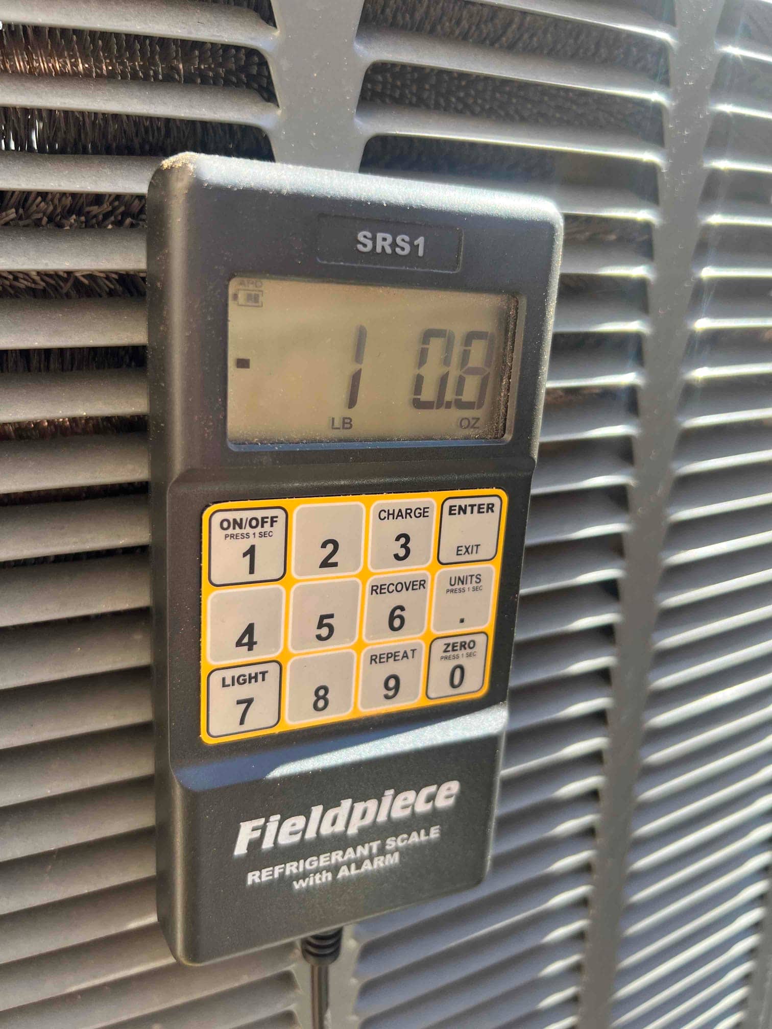 Refrigerant scale shows 1 lb 0.8 oz during R-410A charging beside the outdoor condenser unit.