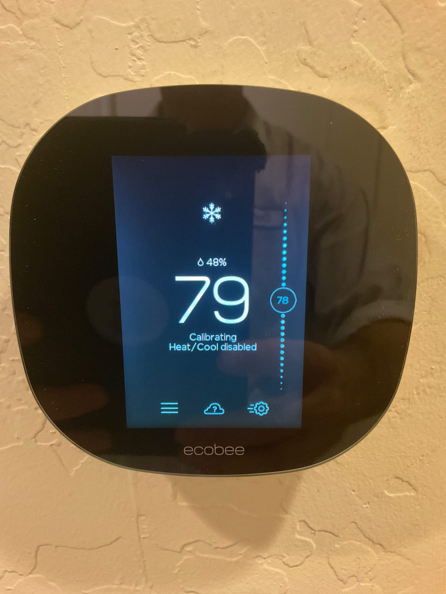 Smart thermostat mounted on interior wall displaying 79 degrees and calibrating status with heating and cooling temporarily disabled.