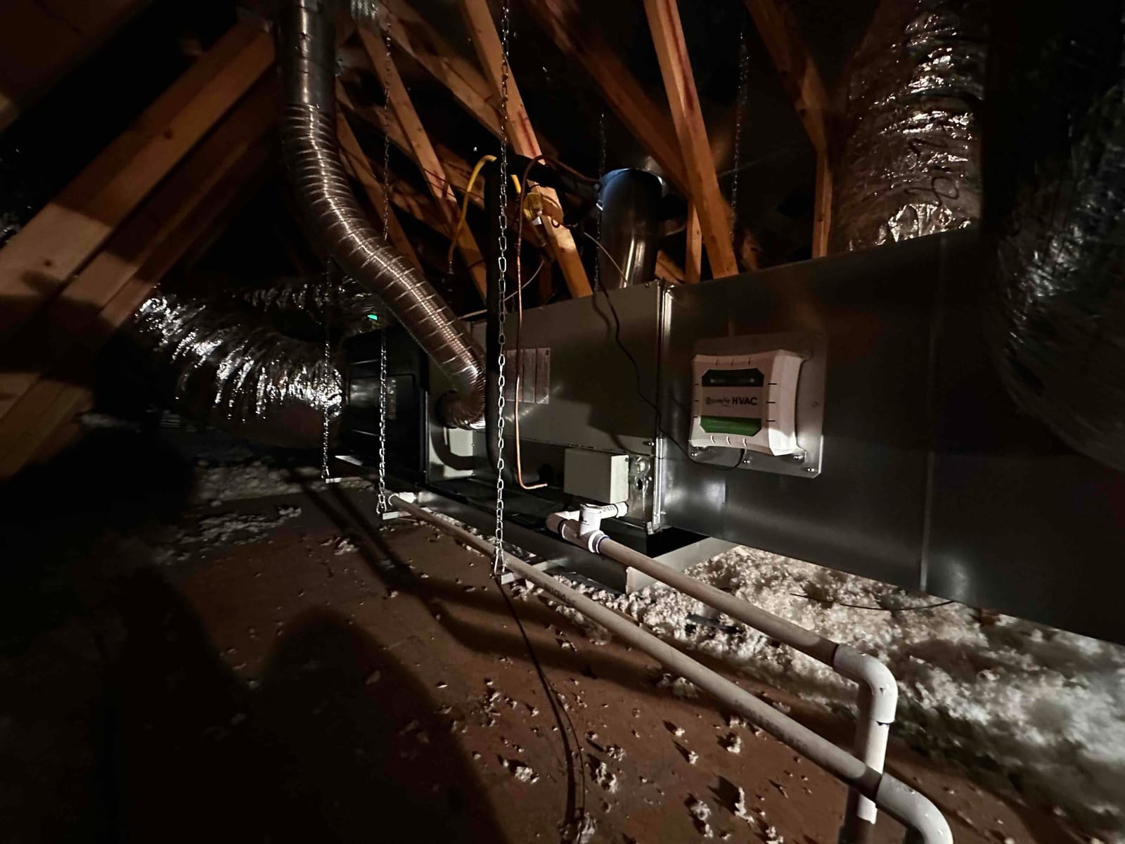 Suspended attic air handler with insulated duct connections and newly installed PVC condensate drain piping routed to the drain line.