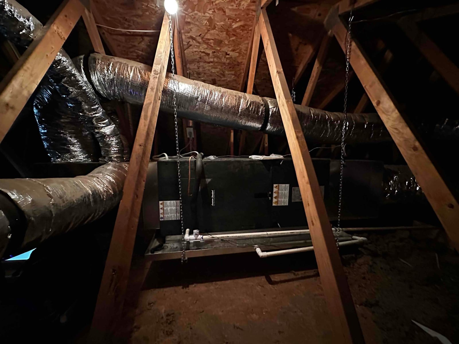 Suspended attic air handler with insulated supply and return ducts connected and PVC condensate drain routed to a secondary safety pan.