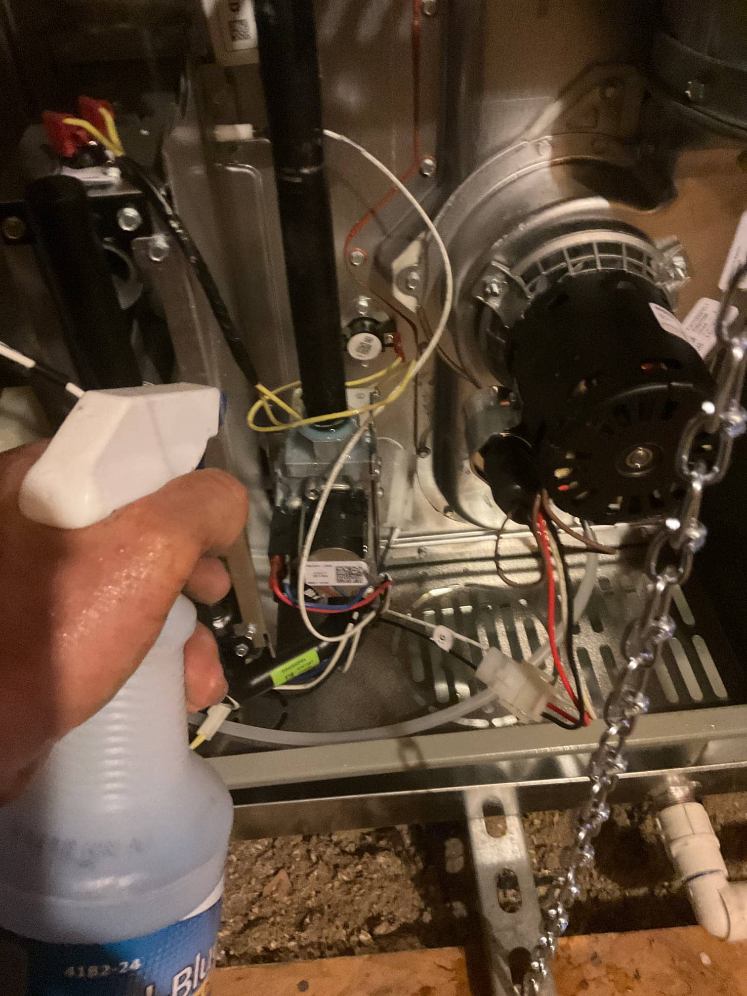 Technician sprays leak-detection solution while inspecting wiring and components inside the furnace cabinet near the inducer assembly.