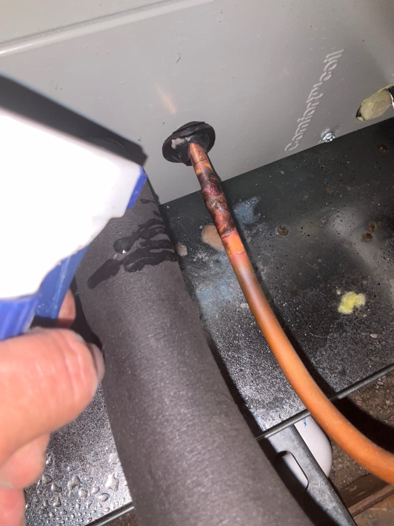 Technician sprays leak-detection solution on insulated suction line and copper liquid line at the air handler penetration.