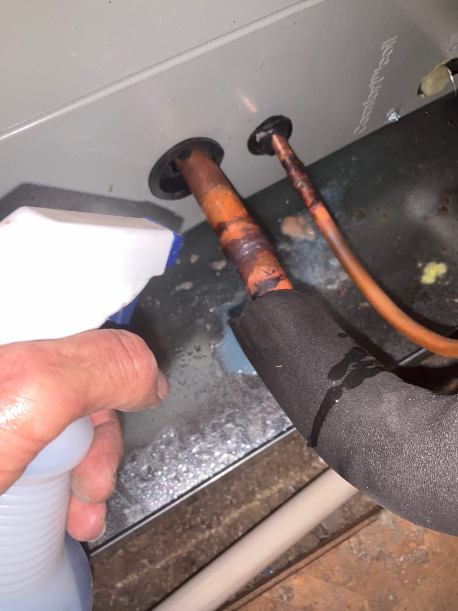 Technician sprays leak-detection solution on newly brazed suction and liquid lines where they enter the air handler cabinet.