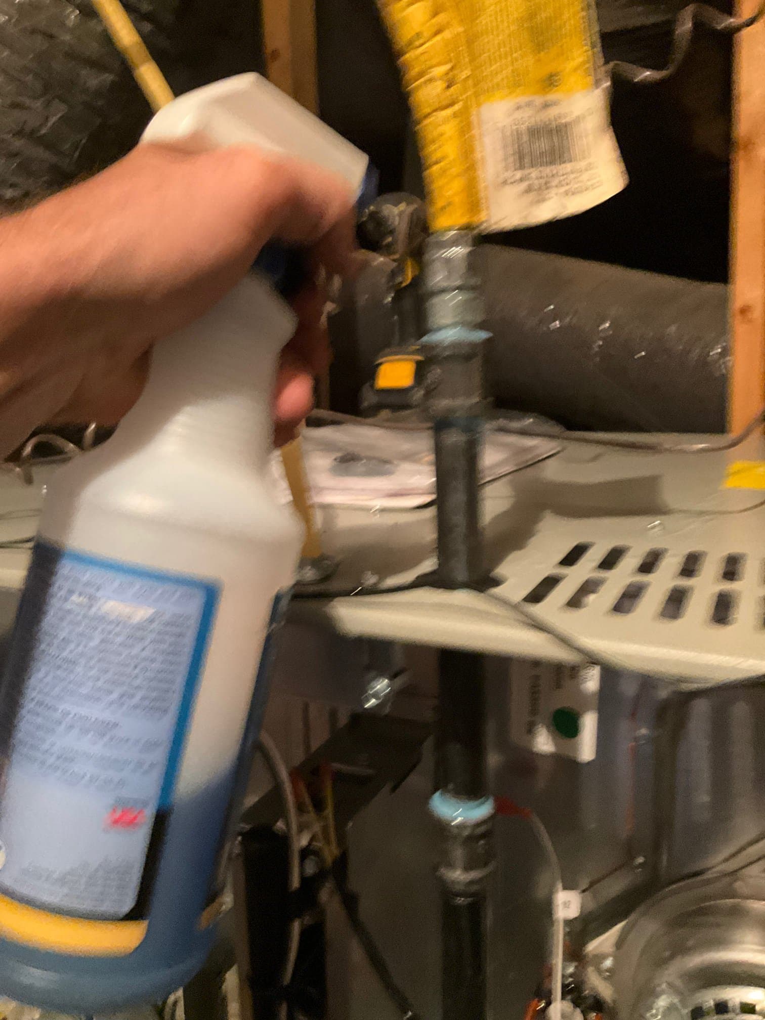 Technician sprays leak detector on a black gas pipe connection near the furnace during installation.