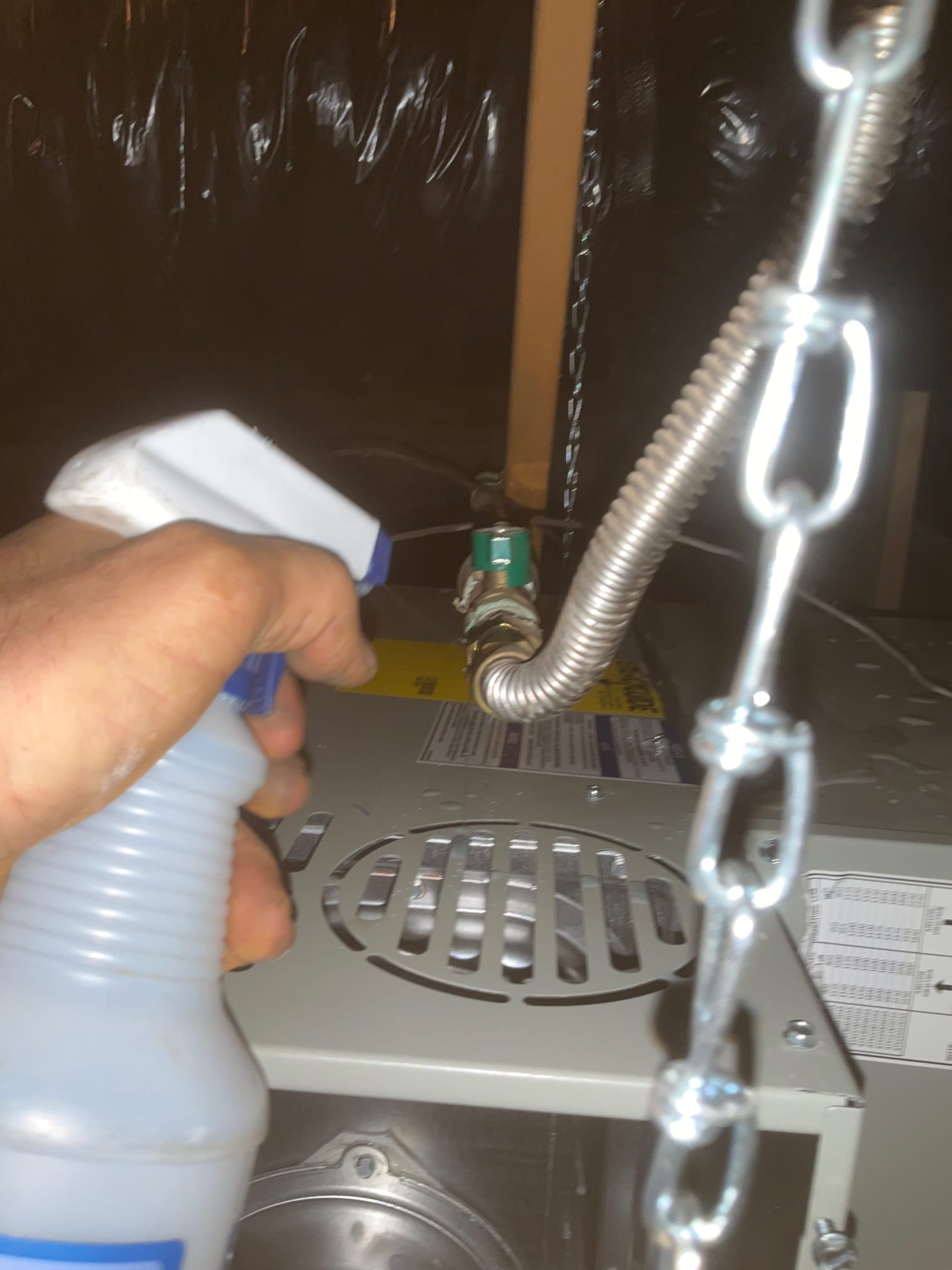 Technician sprays leak detector on a flexible gas connector and shutoff valve at a newly installed furnace.