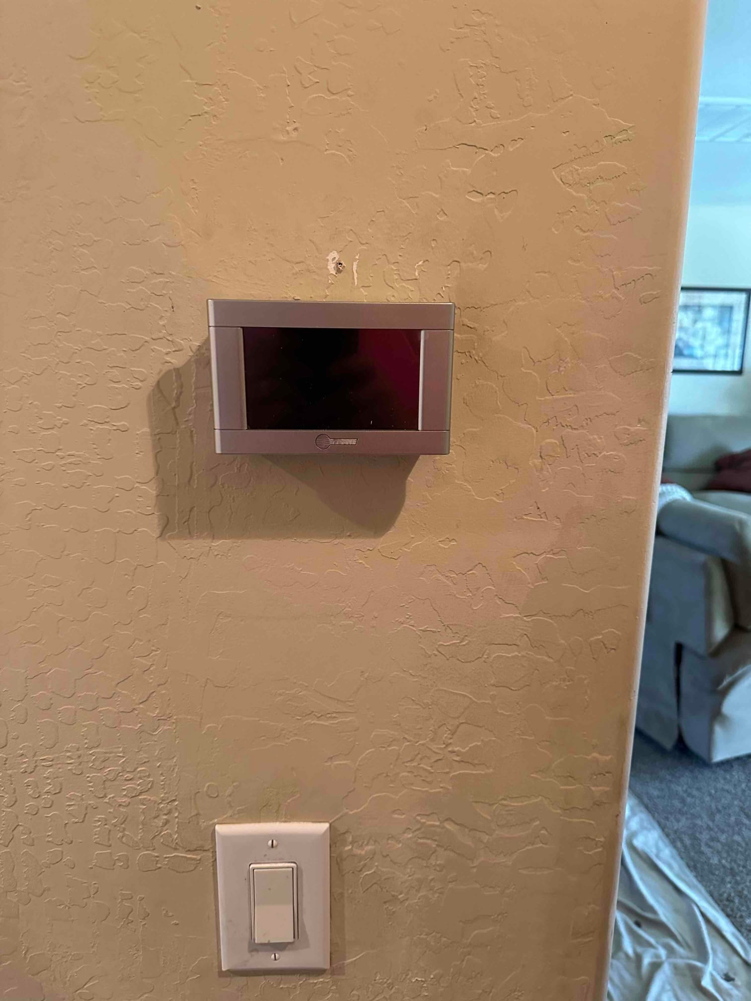 Wall-mounted digital thermostat installed on an interior wall above a light switch during HVAC installation.