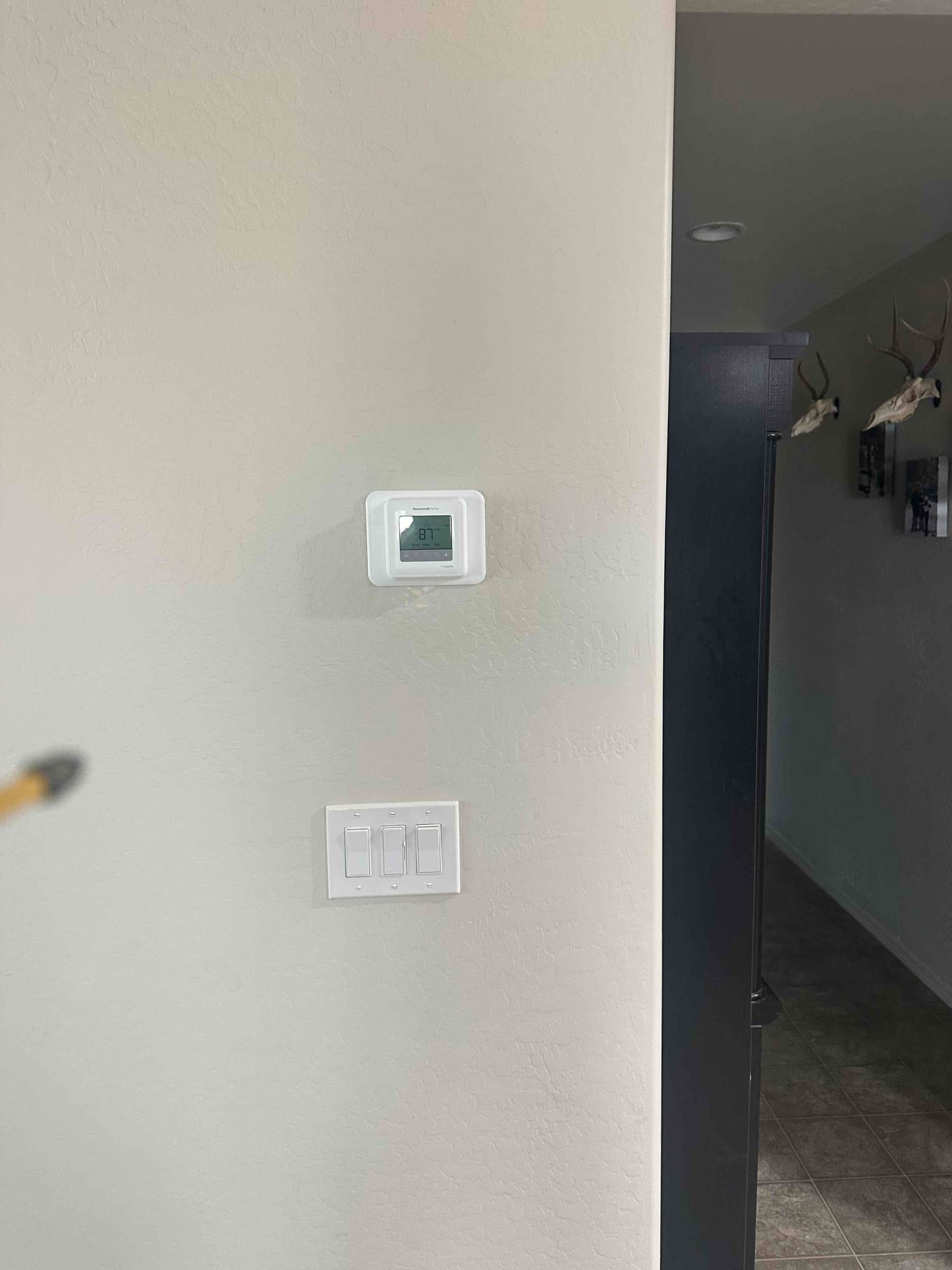 Wall-mounted digital thermostat installed and powered on, with adjacent light switches on the finished interior wall.