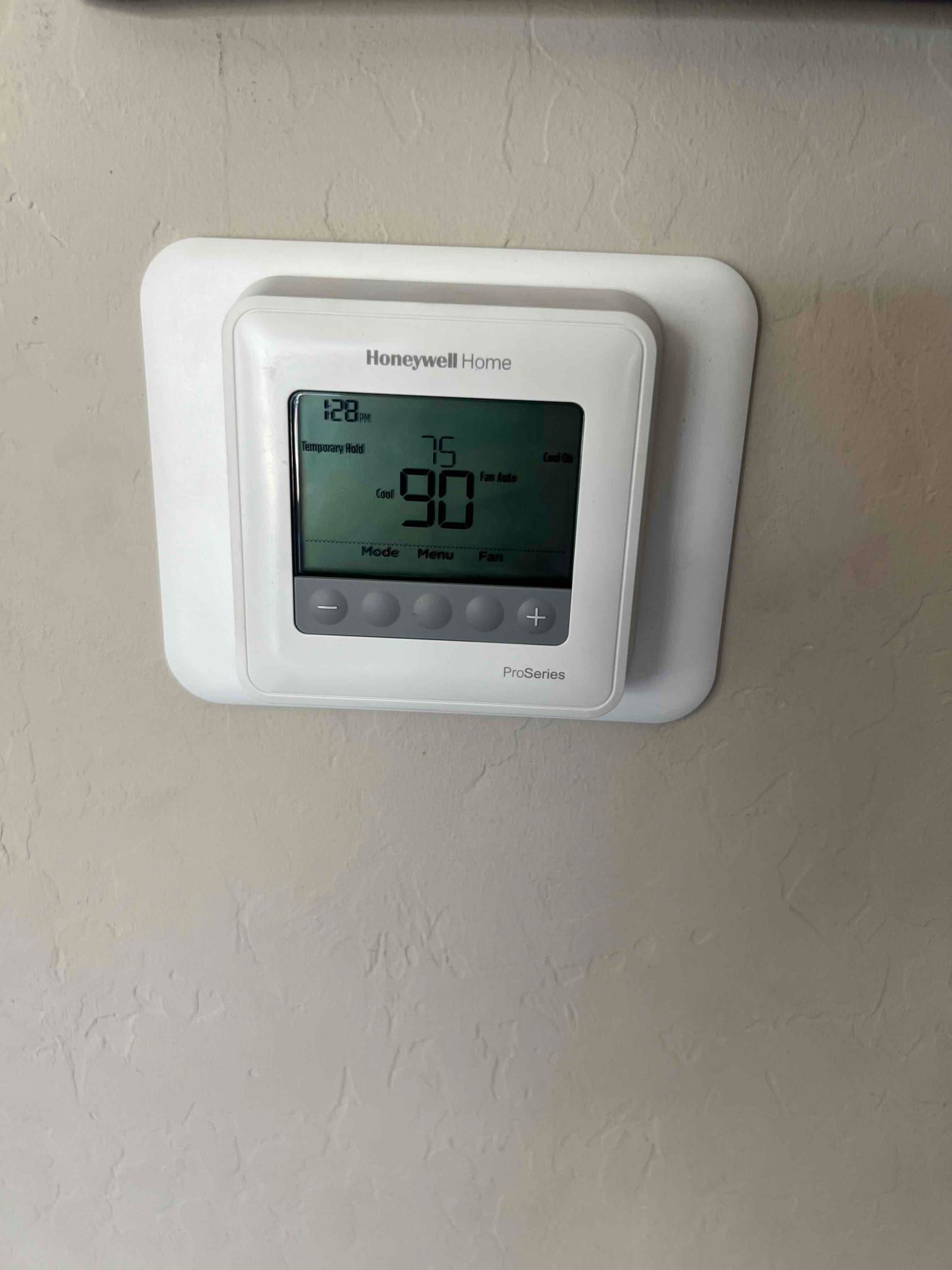 Wall-mounted digital thermostat installed and powered on, displaying current room temperature and cooling setpoint with control buttons.