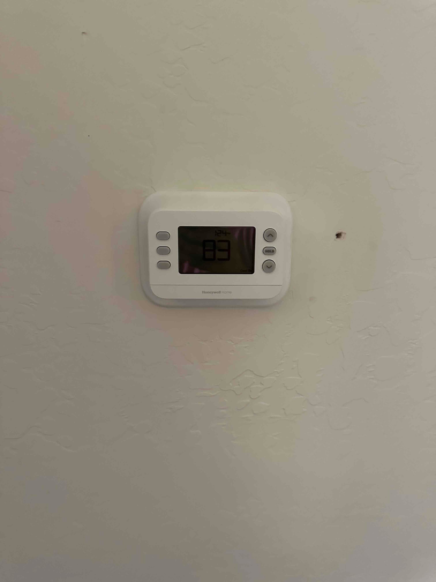 Wall-mounted thermostat installed and powered on, displaying an indoor temperature reading of 83 degrees.