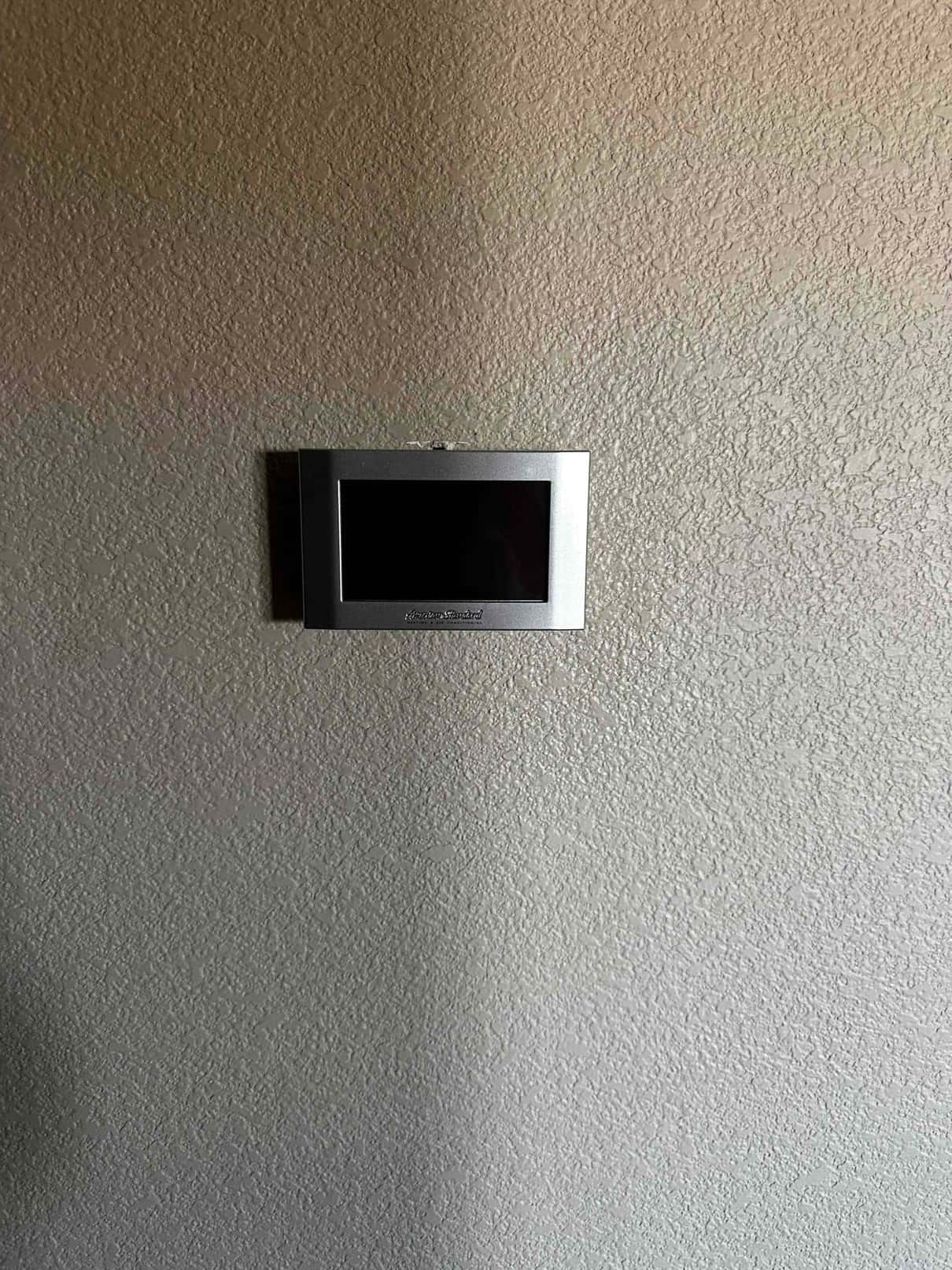 Wall-mounted thermostat installed on textured interior wall with blank display, showing the completed control location for the new system.