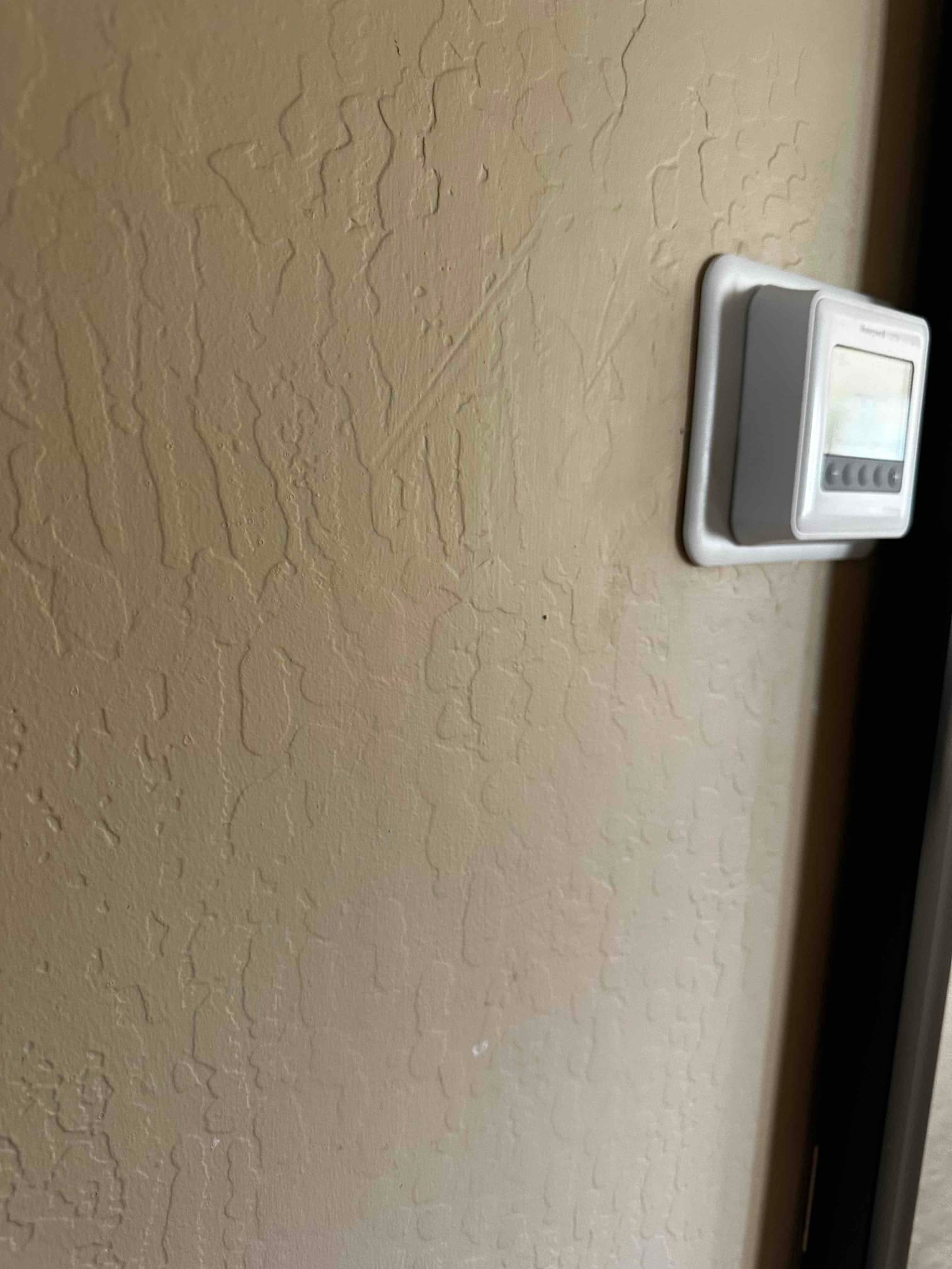 Wall-mounted thermostat with wall plate installed on a textured interior wall near a doorway during HVAC installation.