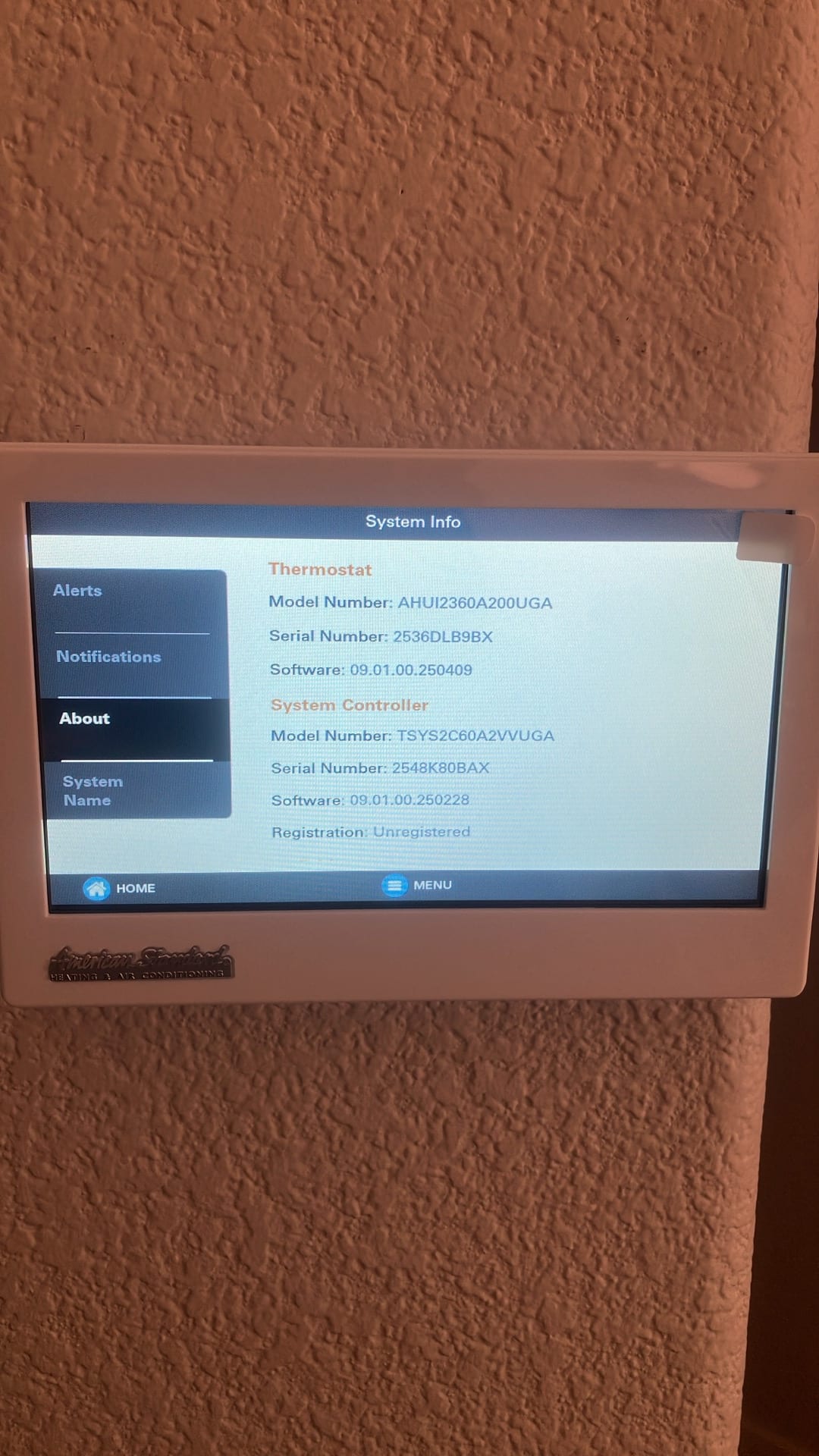 Wall-mounted touchscreen thermostat displays system information menu after installation, showing thermostat and system controller details on the screen.
