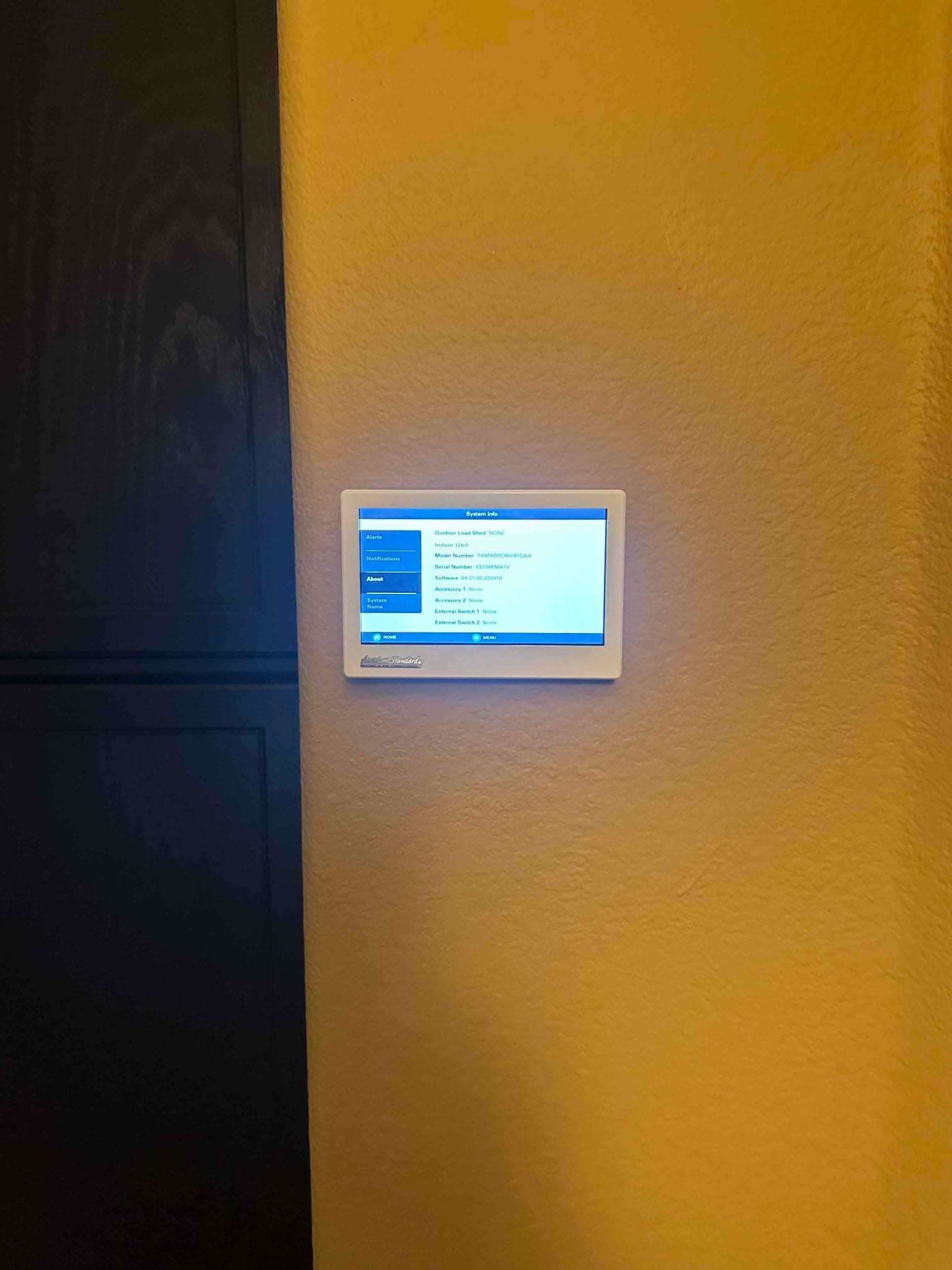 Wall-mounted touchscreen thermostat powered on, displaying system information after the new HVAC installation.