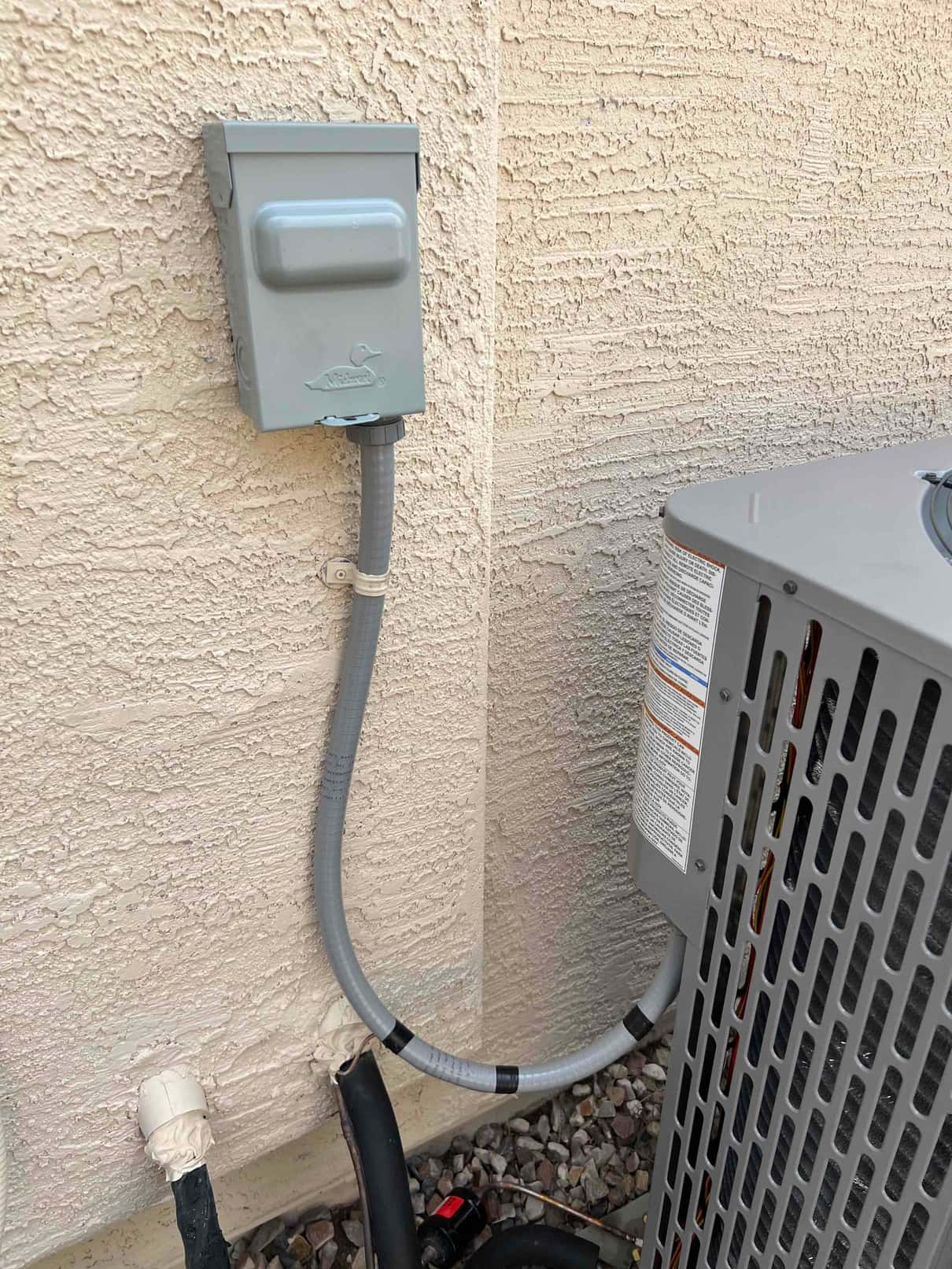 Weatherproof electrical disconnect with flexible conduit connected to the outdoor condenser, alongside insulated refrigerant lines and condensate drains.