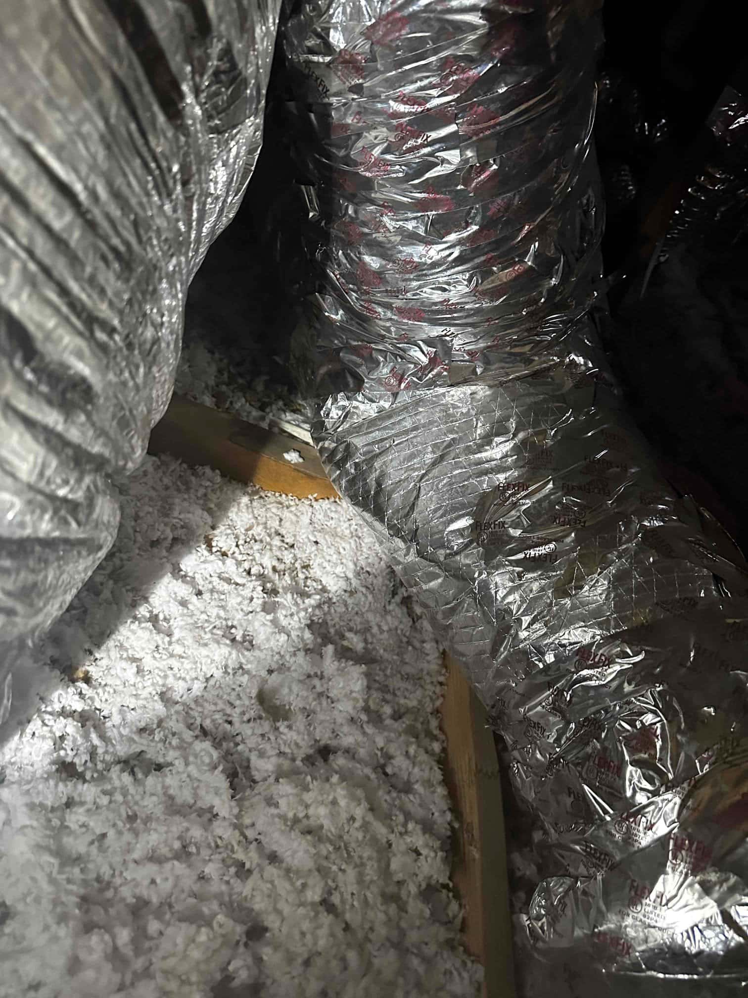 Flexible insulated duct runs in an attic, routed through blown-in insulation with vapor barrier intact and joints taped.
