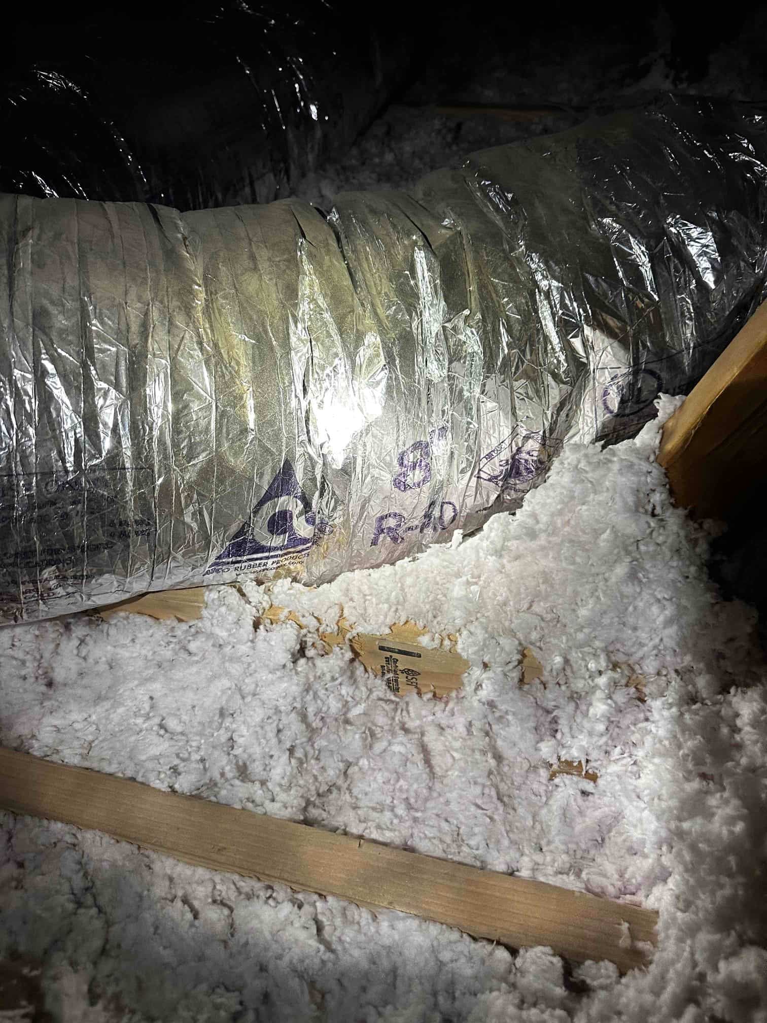 Insulated flexible duct run in the attic laid over blown-in insulation, showing clean vapor barrier and secured routing.