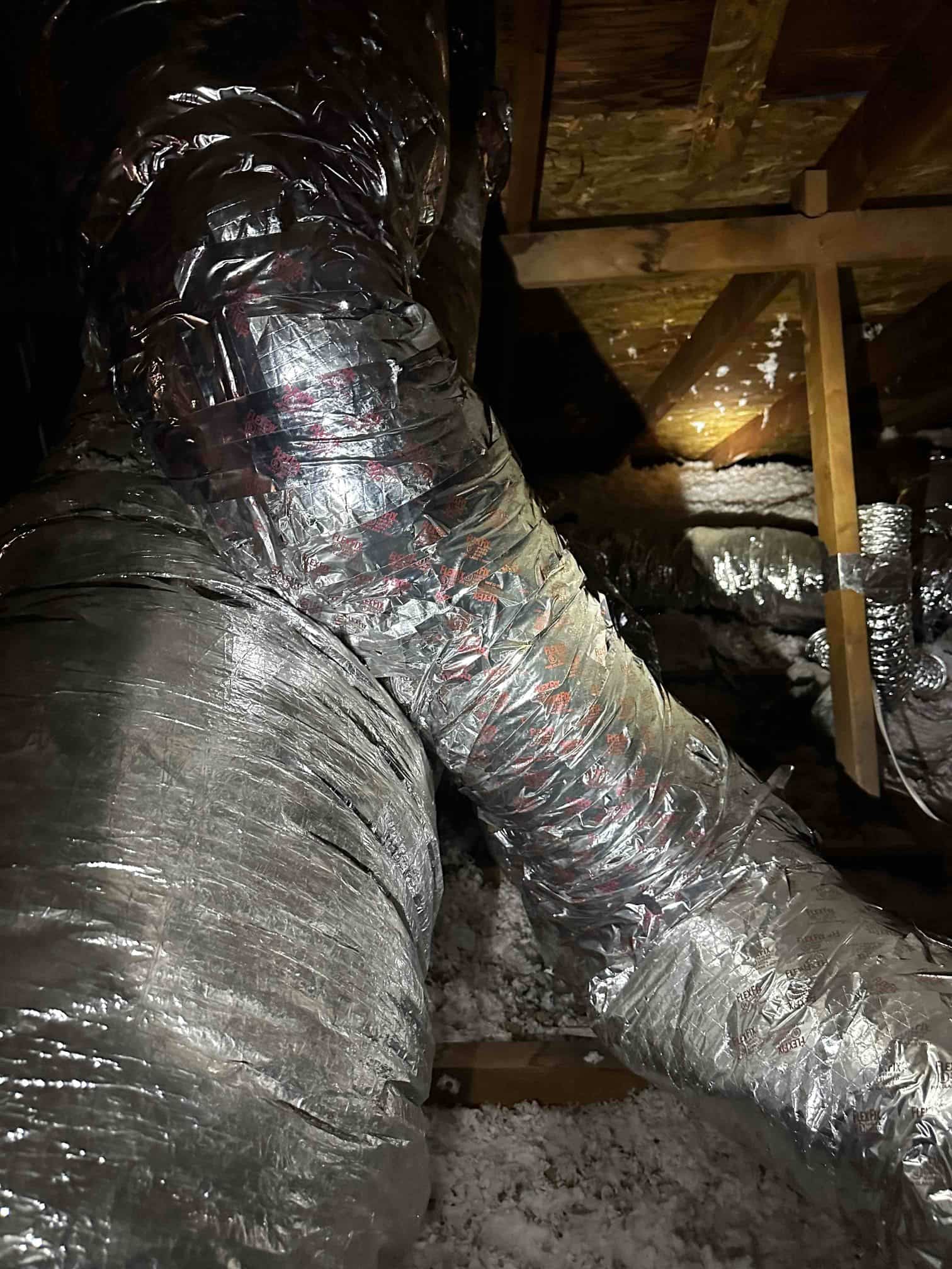 Insulated flexible ducts run through the attic, with a taped wye connection and surrounding blown-in insulation visible.