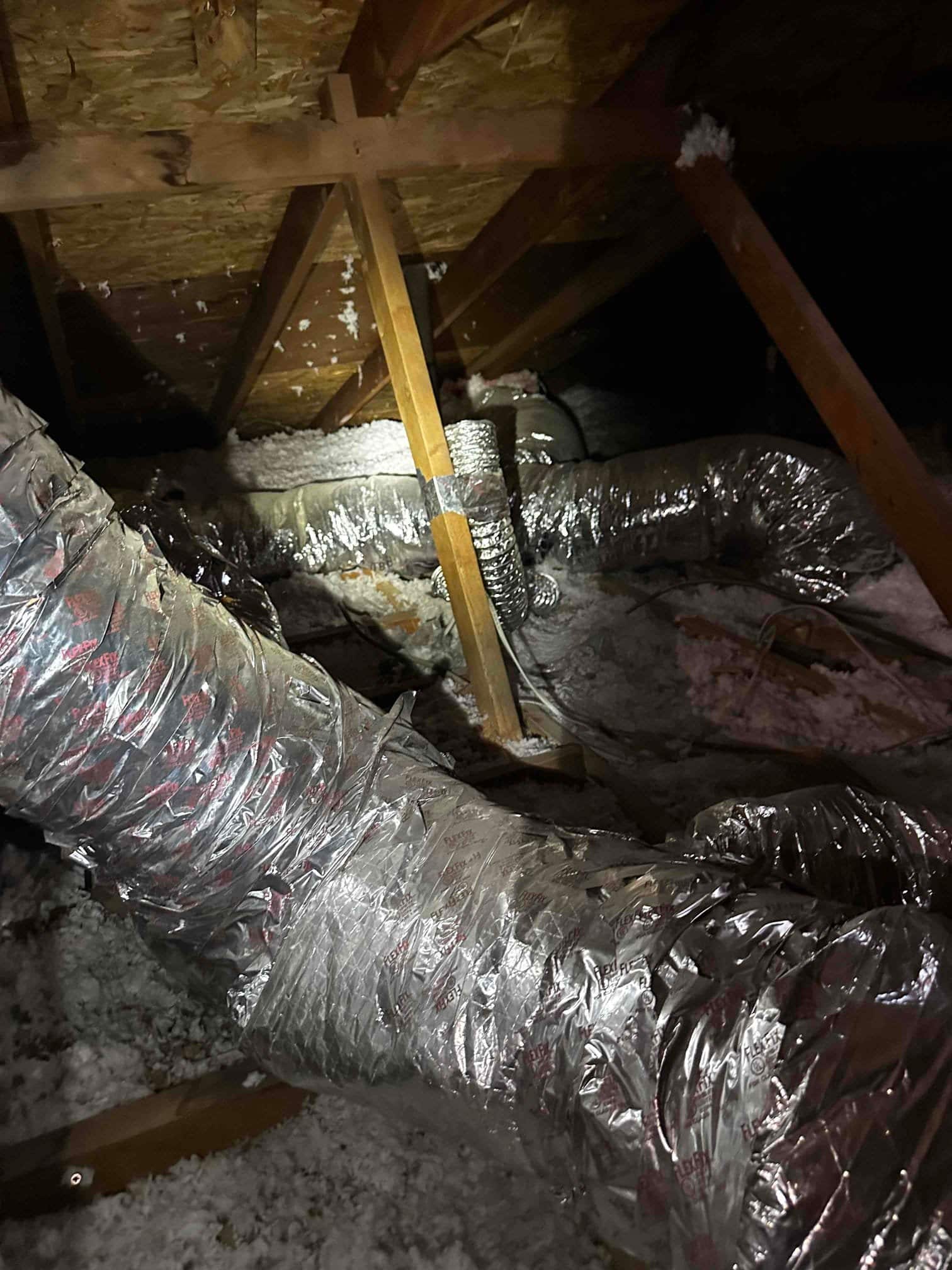 Insulated flexible ductwork routed through an attic, secured and taped at joints amid loose-fill insulation.