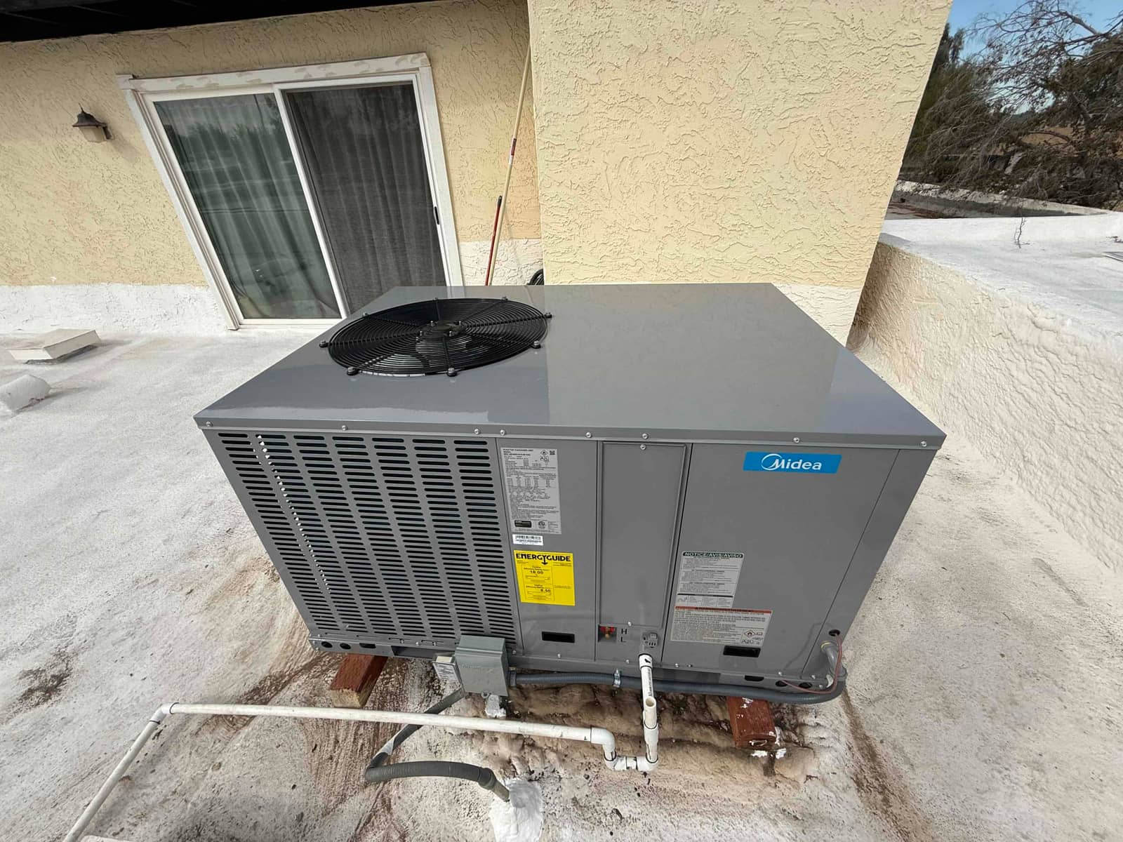 New rooftop package unit set on supports with connected condensate drain, electrical whip, and sealed penetrations at the installation site.