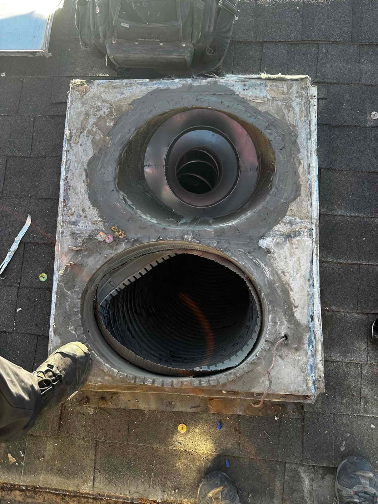 Roof penetration with two round duct openings exposed during rooftop HVAC installation, showing lined ducts and surrounding curb flashing.