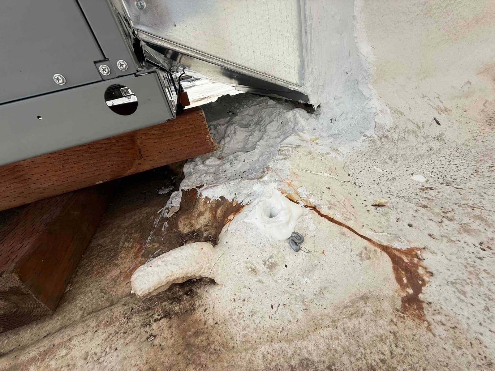 Rooftop package unit curb area sealed with mastic and set on wood shims, showing drain penetration and surrounding roof surface.