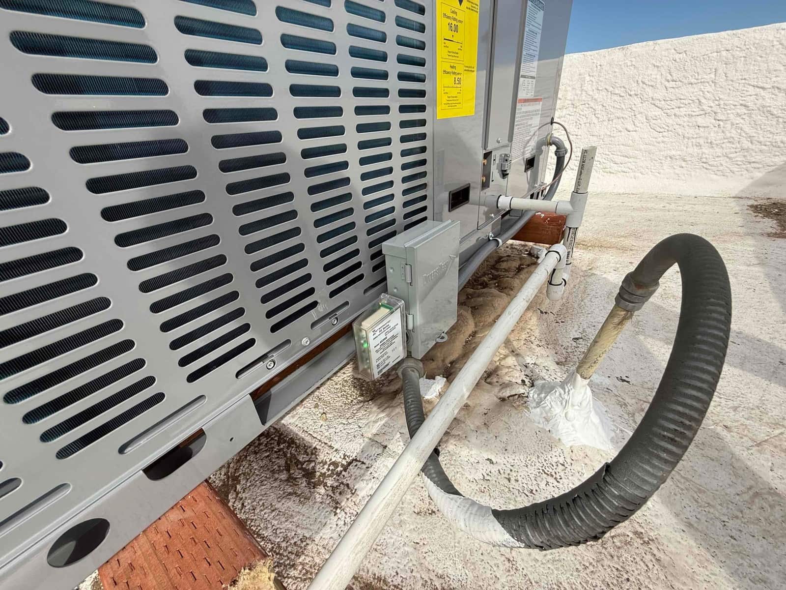 Rooftop package unit installation showing electrical disconnect, condensate drain piping, sealed refrigerant line penetration, and insulated suction line.