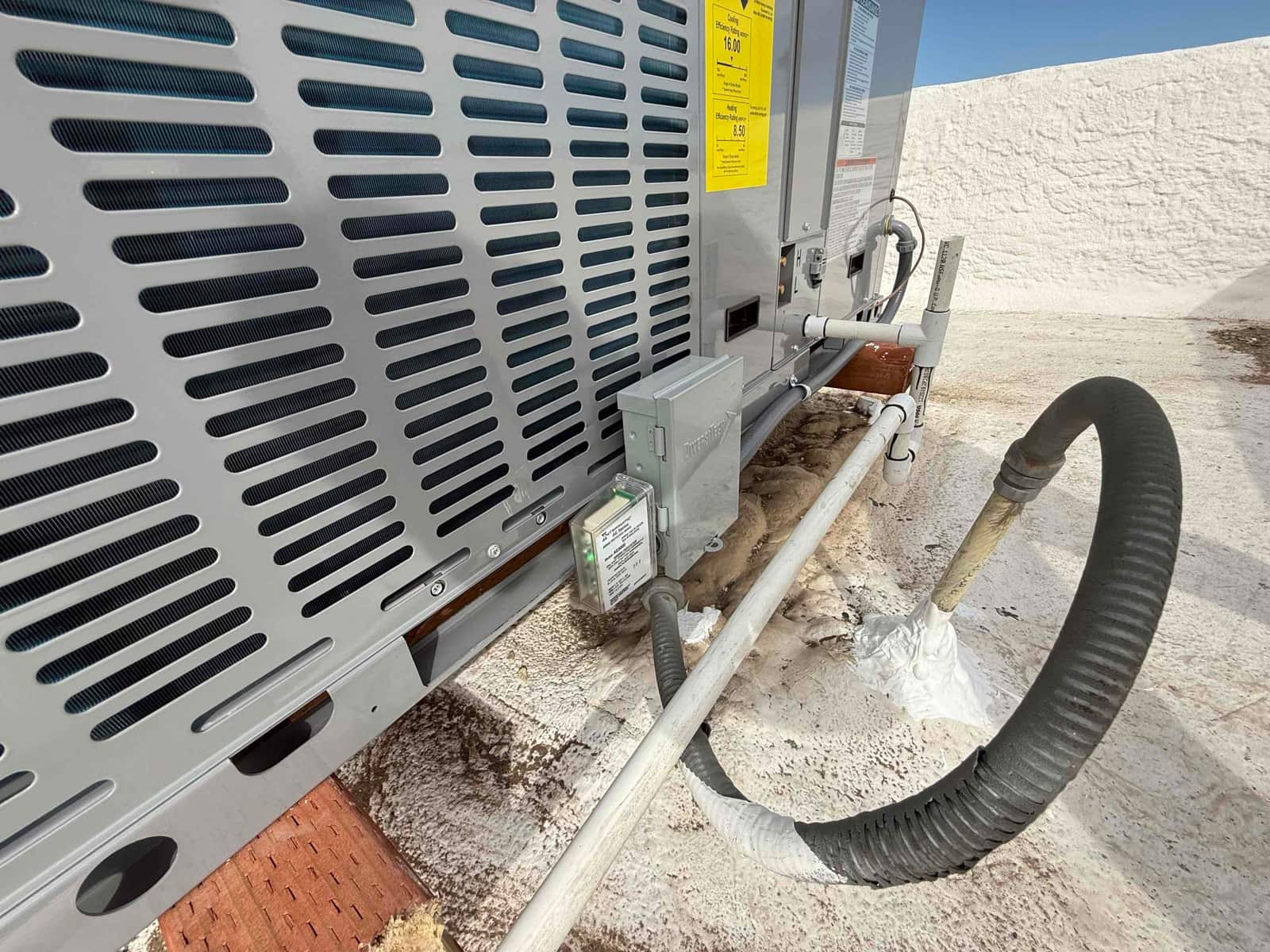 Rooftop package unit installation showing insulated refrigerant line set, condensate drain piping, and mounted electrical disconnect boxes.