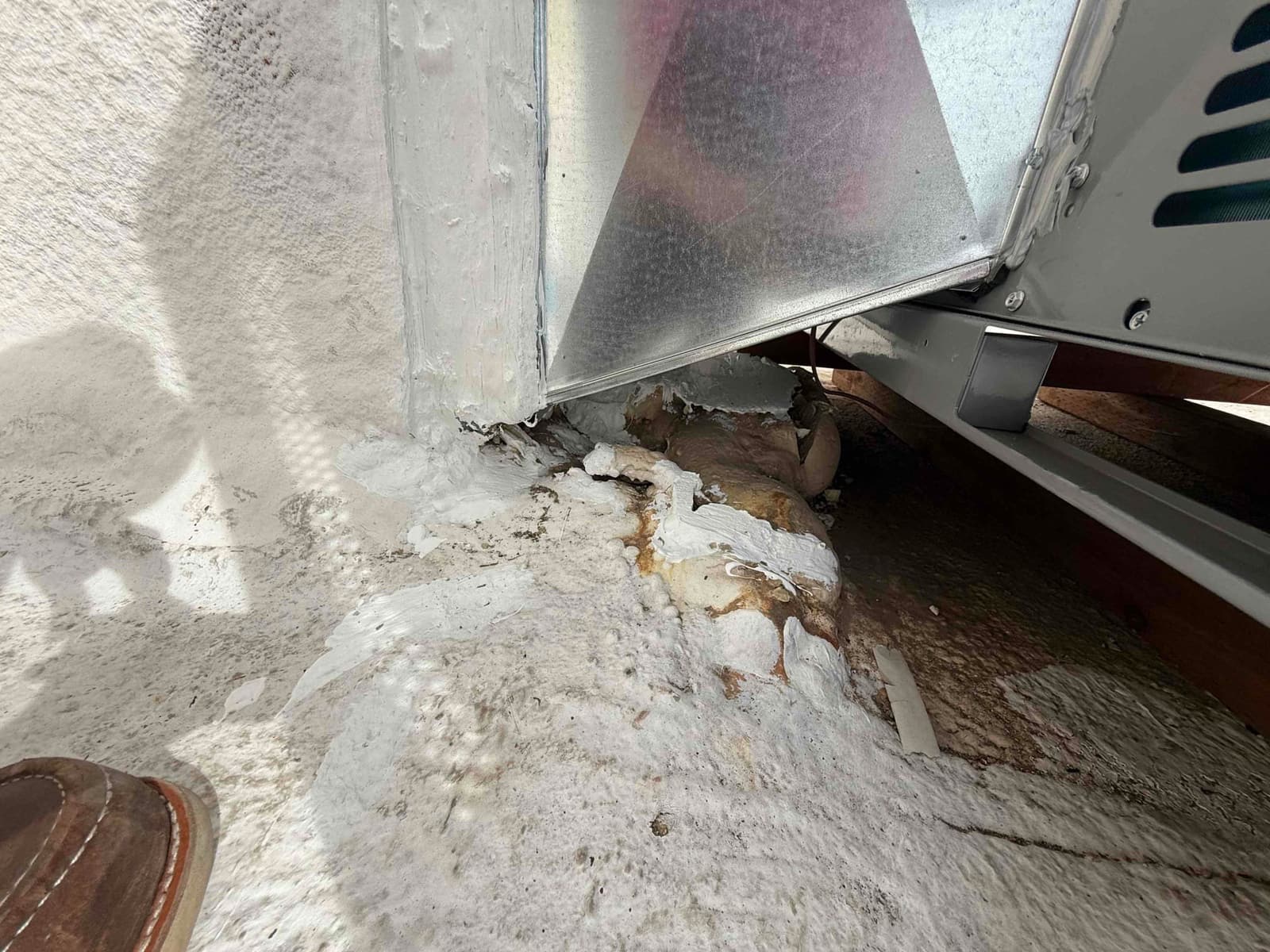 Sealed roof curb and duct connection beneath a rooftop package unit, showing flashing, mastic, and insulation around the penetration.