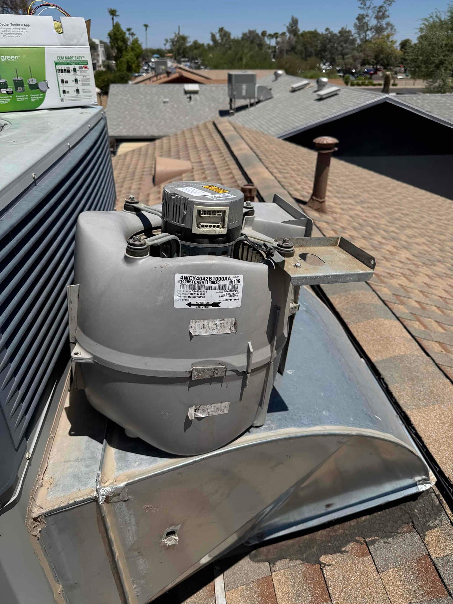 Variable-speed indoor blower motor assembly removed and set on rooftop unit housing, showing housing, motor, bracket, and wiring.