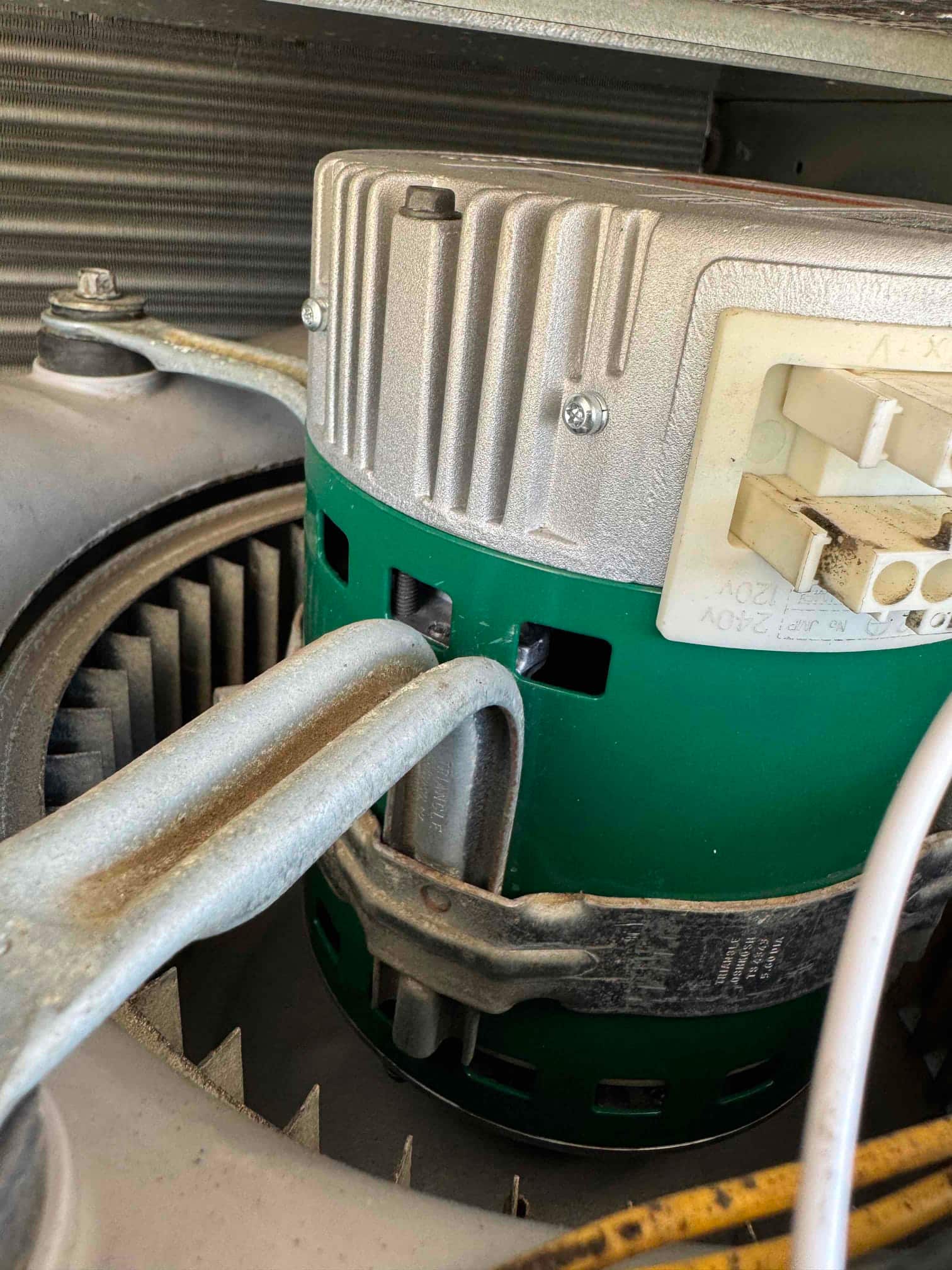 Variable-speed indoor blower motor installed in the air handler, showing wiring connector and mounting strap around the green housing.