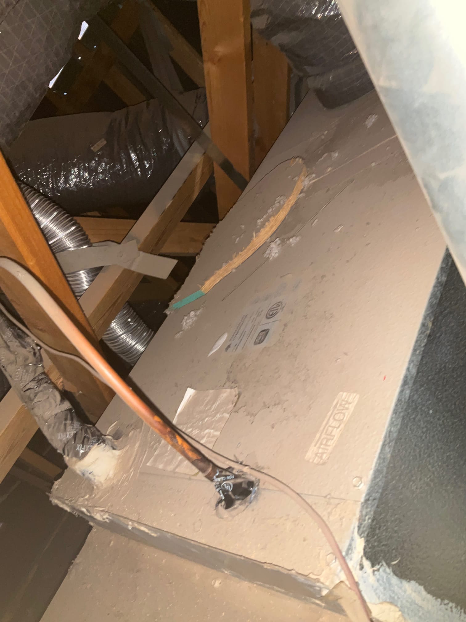 Attic air handler cabinet with copper refrigerant line and insulated flex duct connections visible on top.