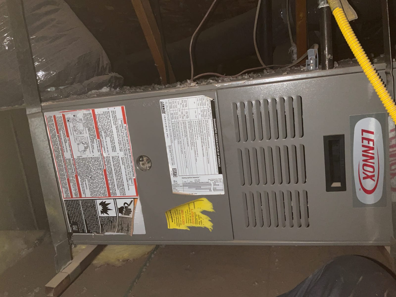 Attic-installed furnace cabinet with service panel labels, louvered door, and flexible yellow gas connector visible along the side.