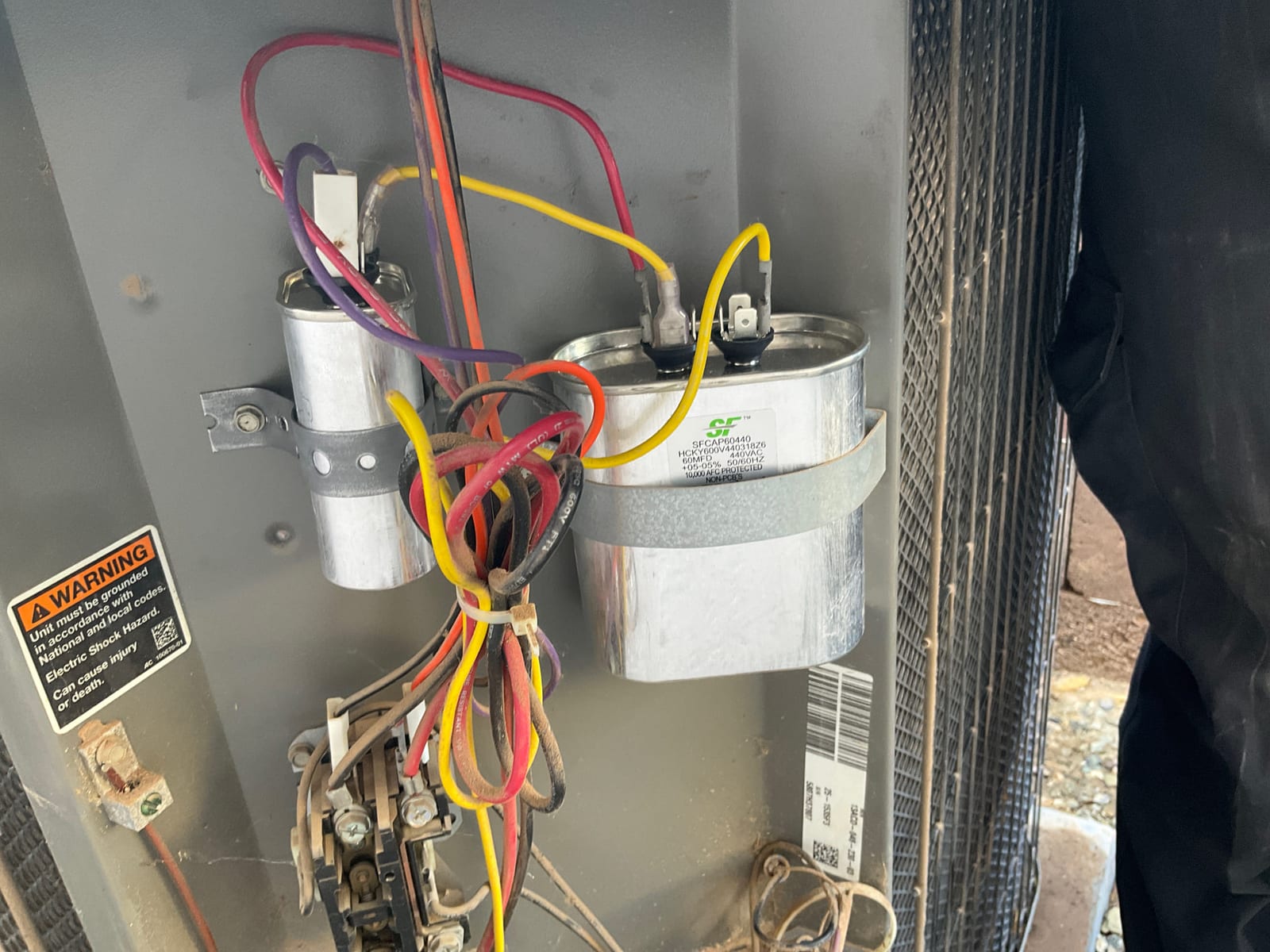 Two capacitors and a contactor mounted inside the outdoor condenser electrical panel with connected wiring.