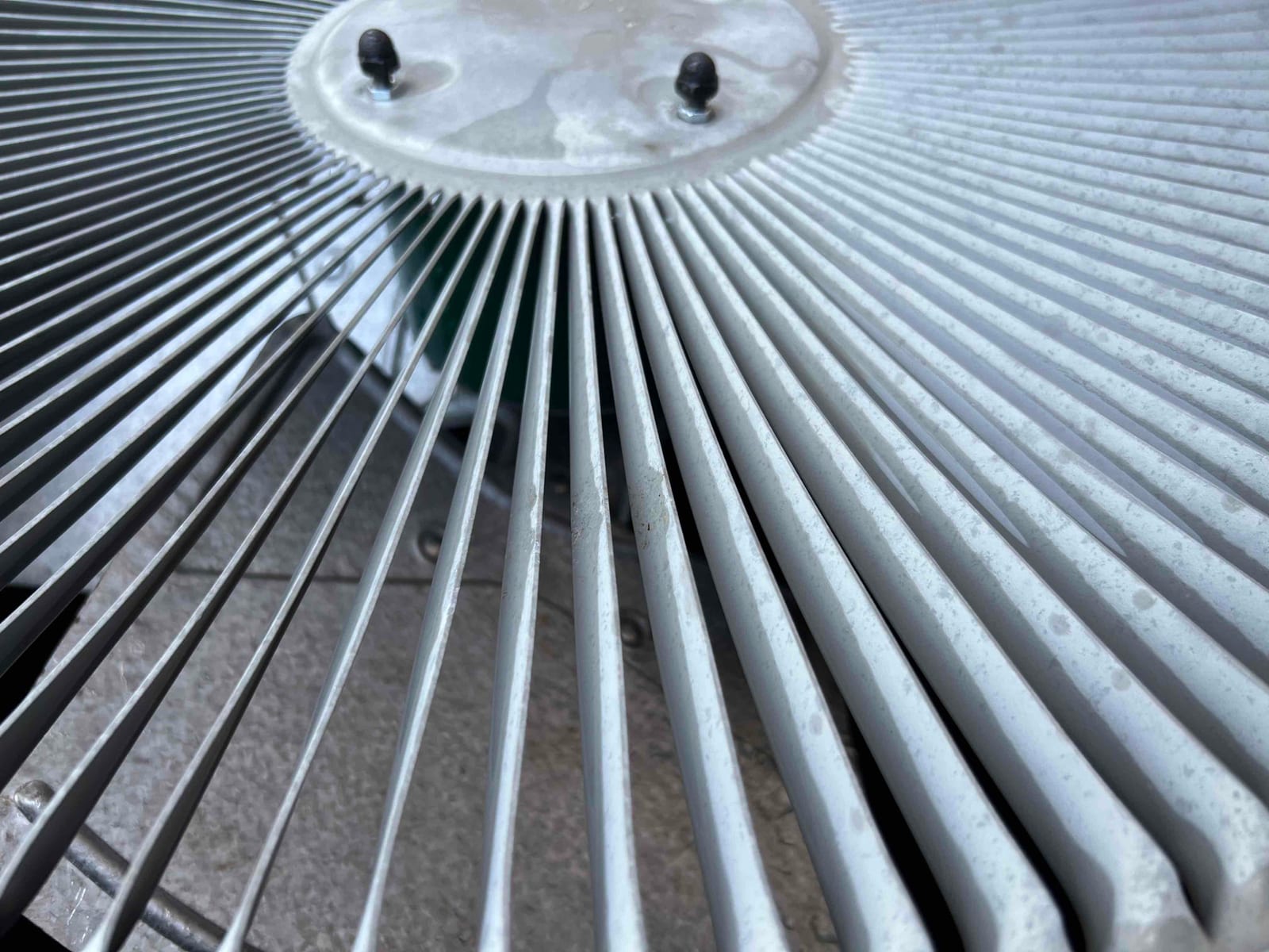 Close-up of an outdoor condenser fan guard and hub with water spots on the grille.