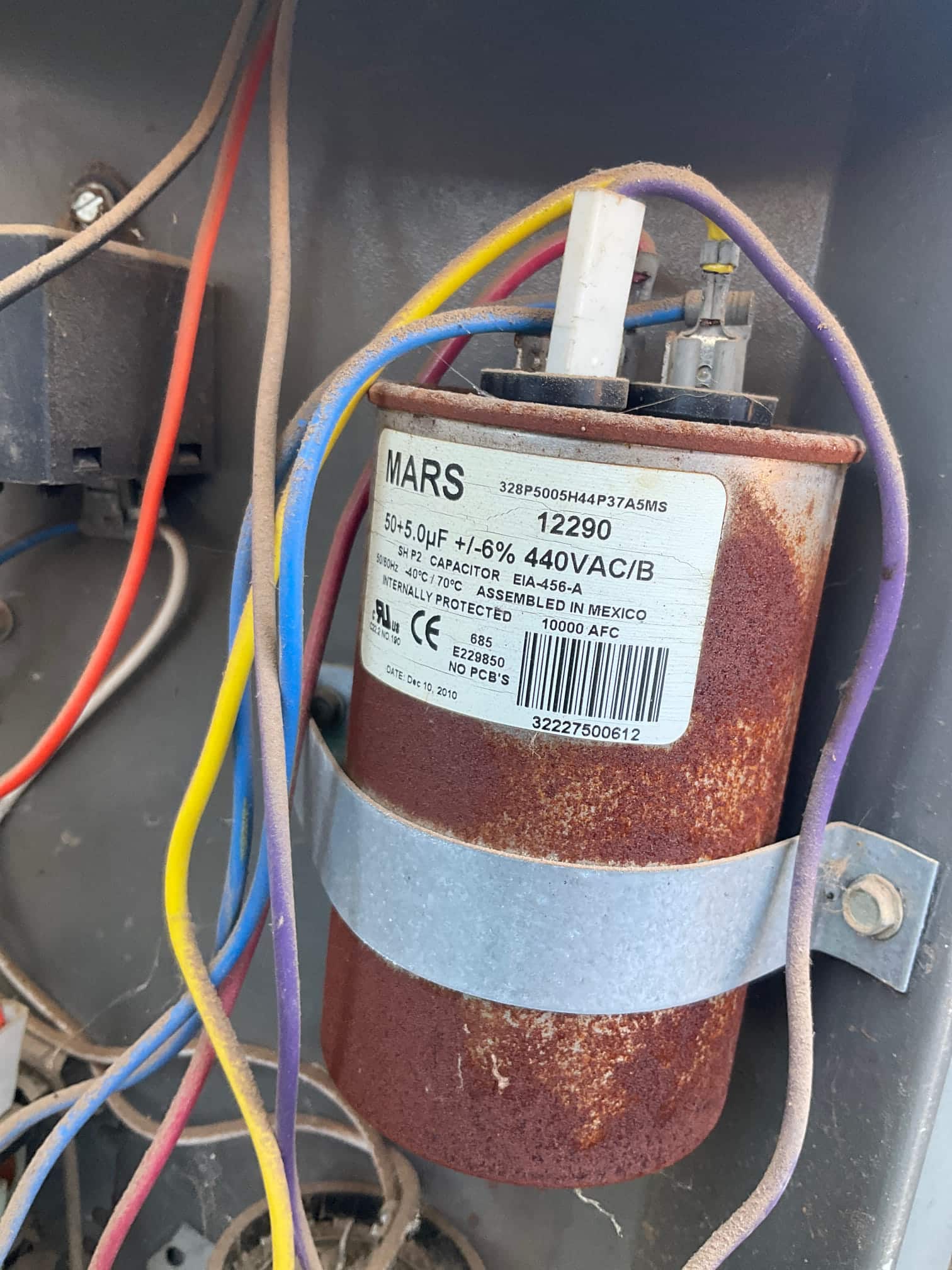Dual-run capacitor with heavy rust on the can, labeled 50/5 μF ±6% 440VAC, with wires connected to its terminals.