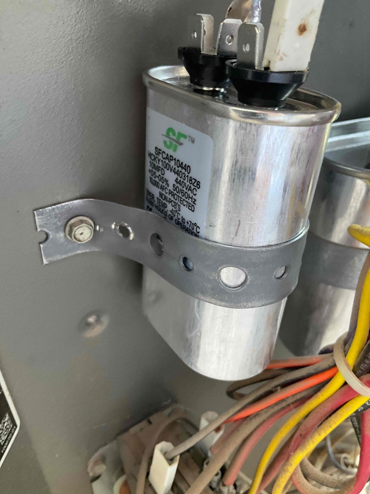 Dual-run capacitor labeled 45/5 μF 440VAC secured with a strap inside the condenser cabinet.