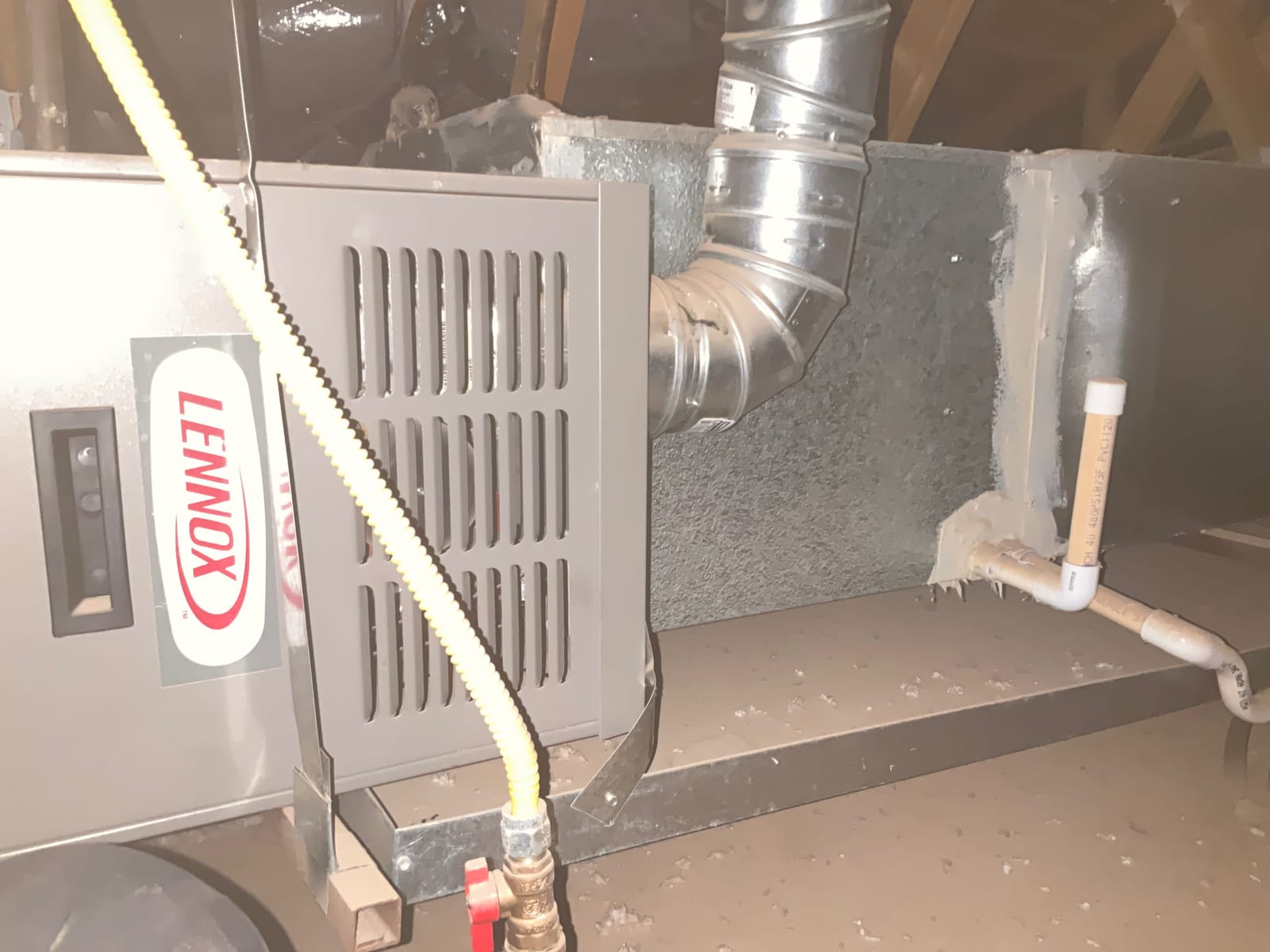 Gas furnace in attic with flexible gas connector, sealed supply plenum, and PVC condensate drain piping visible.