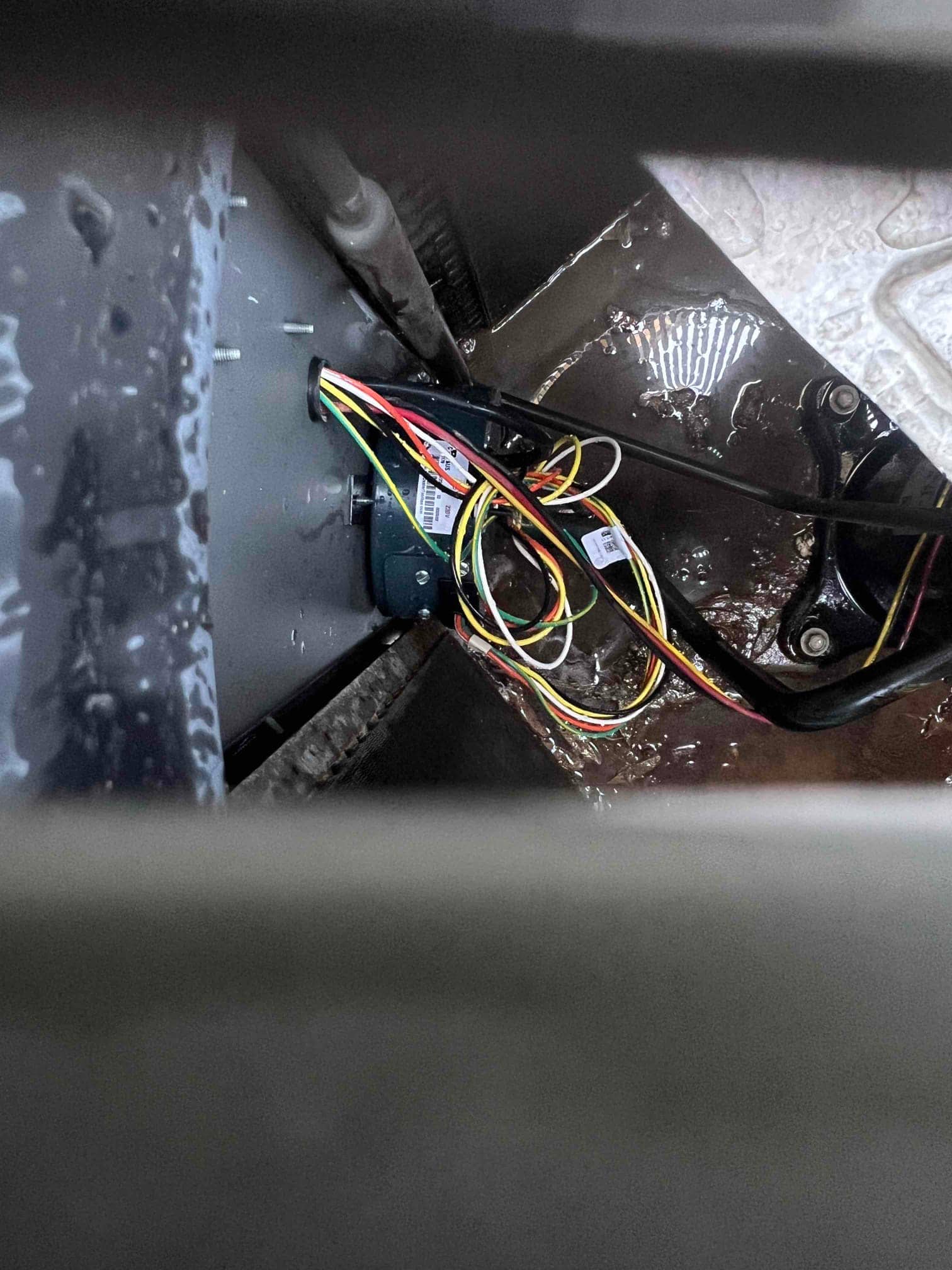 Multicolor wiring harness and small control module inside an HVAC cabinet, with water pooled on the metal base.