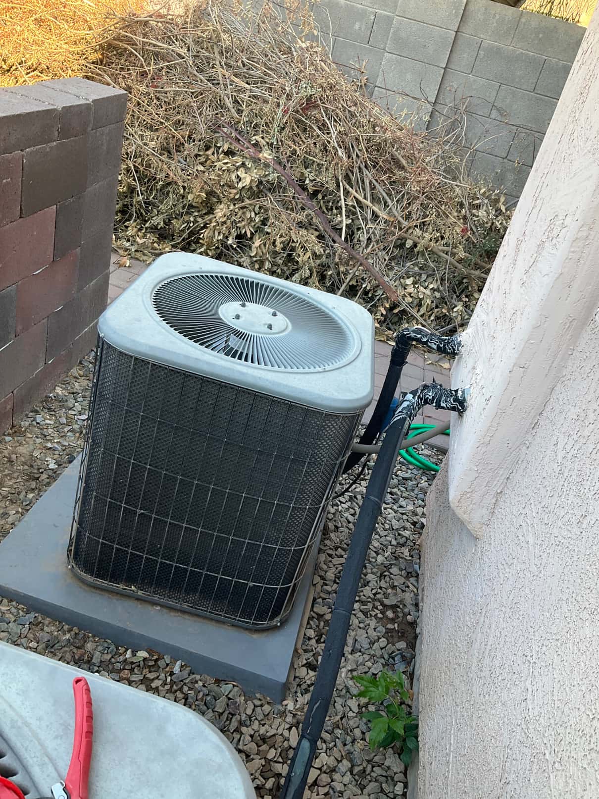Outdoor air conditioner condenser on a concrete pad with insulated refrigerant lines entering the wall.