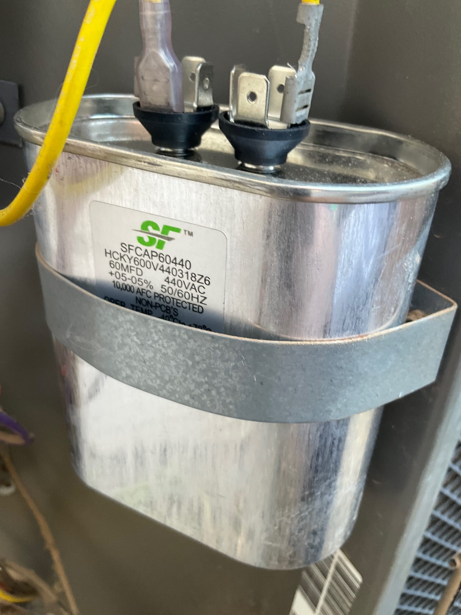 Oval run capacitor strapped in place with two terminals connected; label shows 60MF and 440VAC rating.