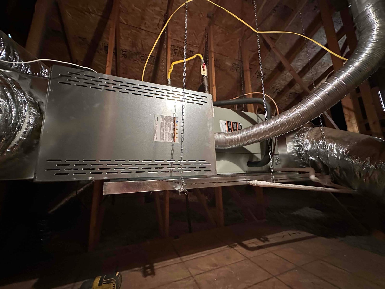 Air handler suspended from joists with chains, connected to insulated ductwork and condensate drain piping in the attic.