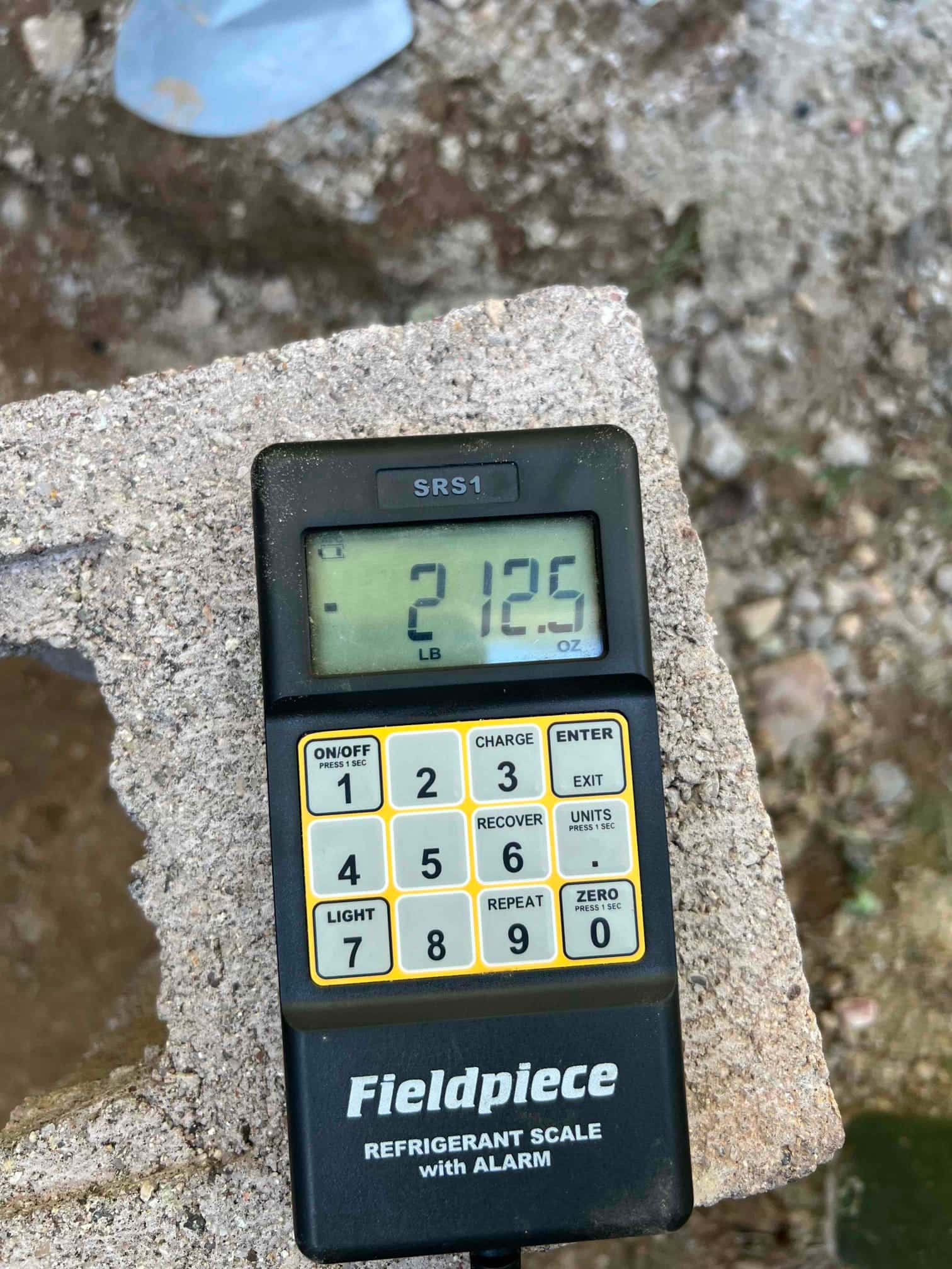 Digital refrigerant scale on a block shows 21.25 pounds during charging work at the installation site.