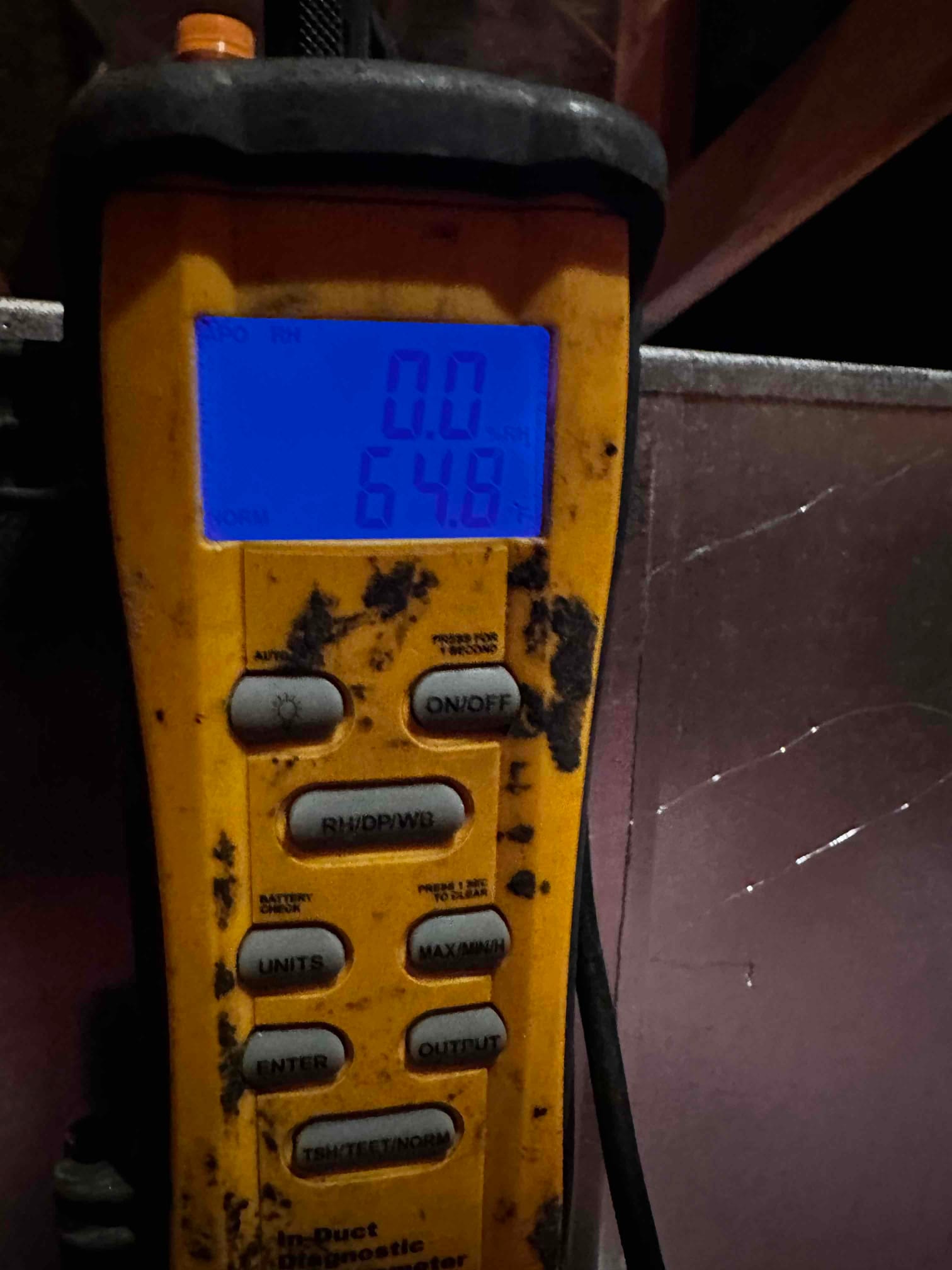 Digital thermometer shows 64.8°F while measuring air temperature near the duct during system commissioning.