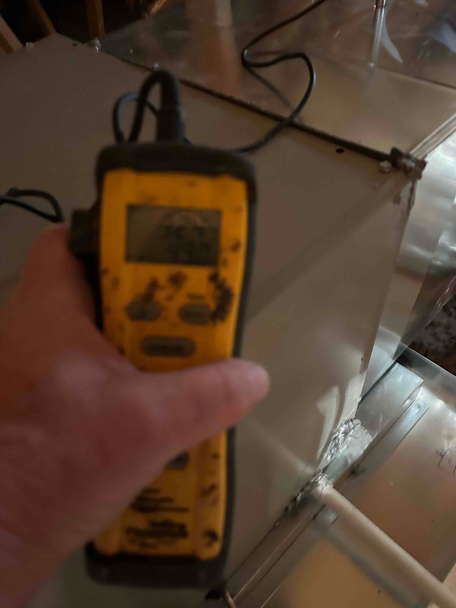 Handheld digital thermometer measuring air temperature at the duct near the furnace during commissioning checks.