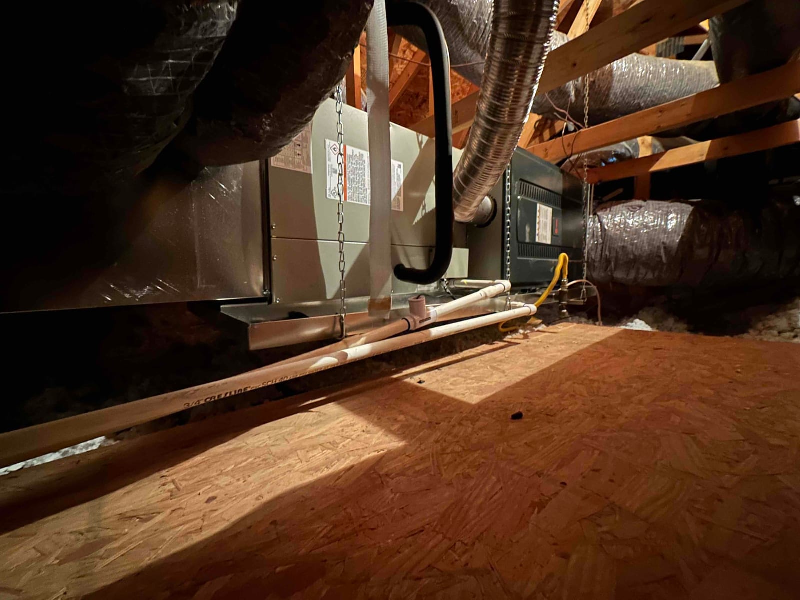 New attic air handler and furnace assembly hung with chains, connected to flexible ductwork, condensate drain piping, and gas line.