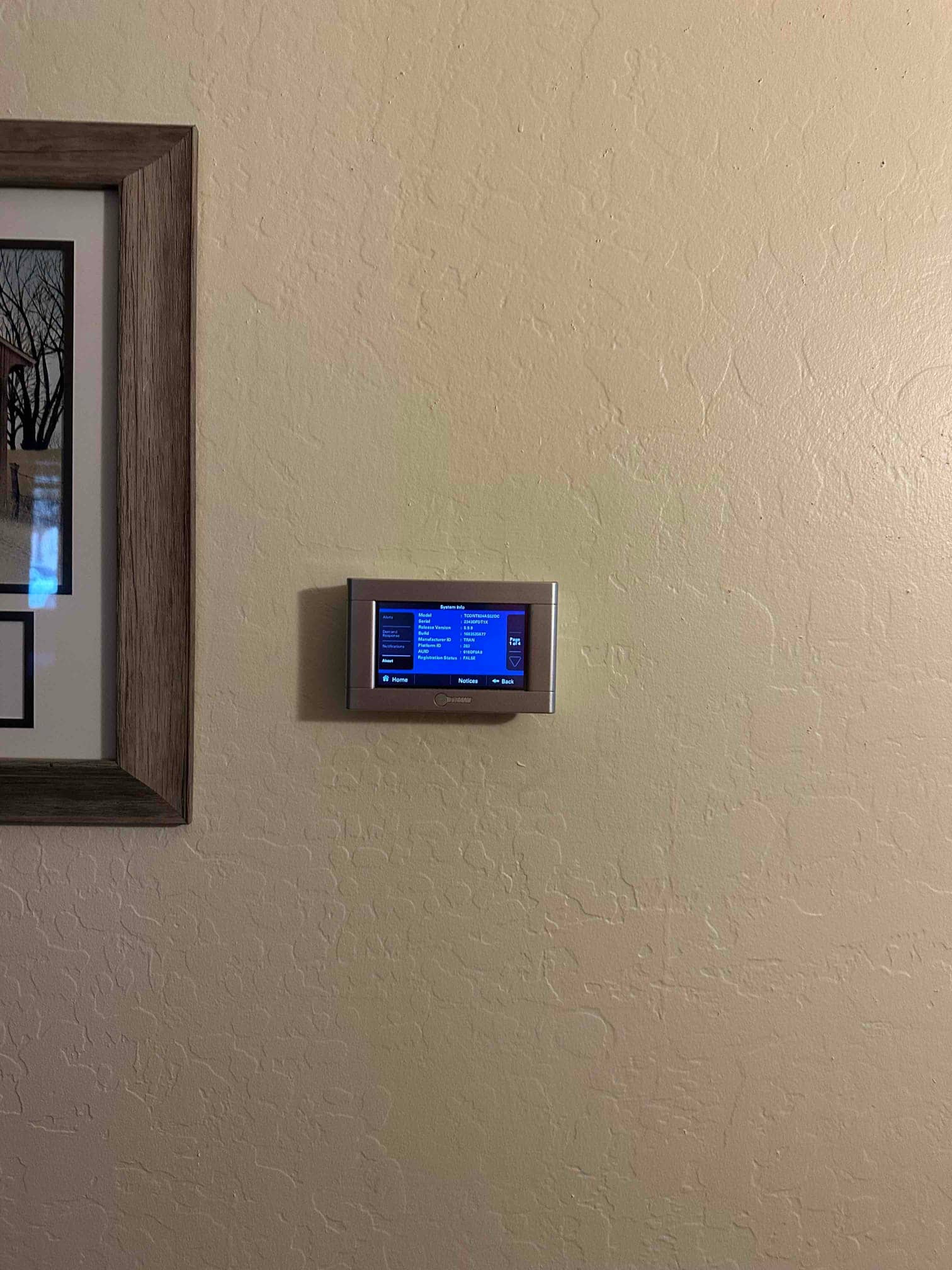 Wall-mounted smart thermostat installed and powered on, displaying its home screen as part of the new HVAC system.