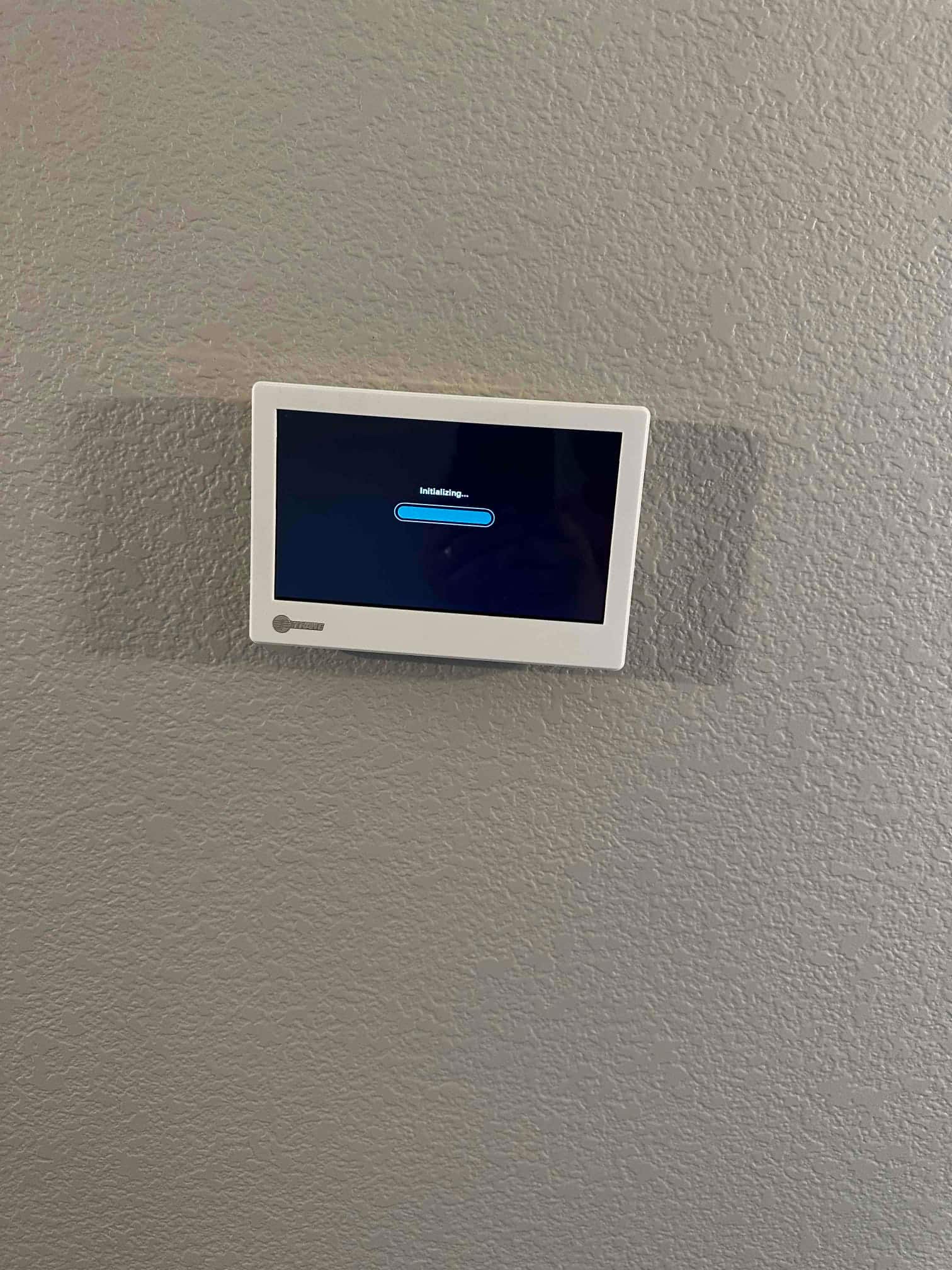 Wall-mounted touchscreen thermostat powers on with an initializing screen after installation and wiring at the new system.