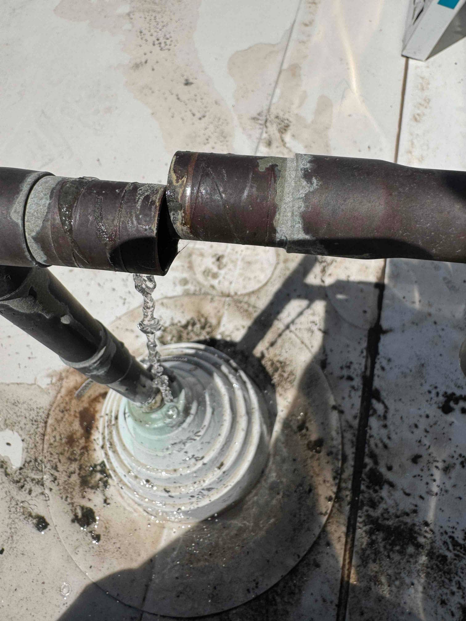 Broken copper condensate drain line with water flowing from the open end onto a roof drain fitting.